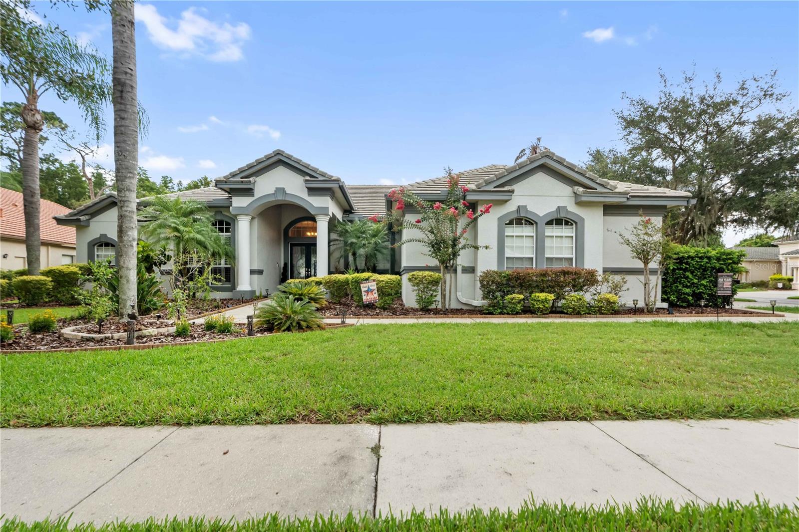 Welcome to 21127 Lake Vienna Drive, an exceptional executive residence in the highly sought-after gated community of Sunset Lakes. Perfectly positioned on a picturesque corner conservation lot, this impressive Hannah Bartoletta Dartmouth II model offers 3,503 square feet of thoughtfully designed living space, featuring 4 bedrooms, 3 full bathrooms, a powder bath, a private office, formal living and dining rooms, an oversized side-entry three-car garage, and the highly desirable optional extended lanai.From the moment you arrive, the stately portico entrance with elegant columns and decorative leaded-glass double doors sets the tone for the luxury that awaits inside. Soaring 12-foot ceilings, hand-scraped hardwood floors, crown molding, graceful archways, plantation shutters, and exquisite architectural details create a timeless and sophisticated atmosphere throughout.Designed with both everyday living and entertaining in mind, the open floor plan features a desirable three-way split bedroom layout that provides exceptional privacy for family and guests. The spacious office is conveniently located just off the foyer, making it ideal for working from home.The gourmet kitchen is beautifully appointed with rich 42-inch cabinetry with display space above, granite countertops, a stunning tile backsplash, stainless steel appliances, a built-in microwave, center island, breakfast bar with pendant lighting, and a separate casual dining area. Filled with natural light, the kitchen and breakfast nook overlook the expansive family room, where two sets of pocketing four-panel sliding glass doors seamlessly blend indoor and outdoor living.
Step outside to your private backyard retreat featuring a screened, heated pool with a sun shelf, elegant vessel-style waterfall, and an expansive L-shaped travertine lanai designed for year-round entertaining. The peaceful conservation backdrop and spacious fenced yard create the perfect setting for relaxing or hosting family and friends.The luxurious owner's suite is a true sanctuary, featuring double-door entry, beautiful hand-scraped hardwood flooring, private lanai access, a generous walk-in closet, and an elegant spa-inspired bath complete with dual vanities, a dedicated makeup area, garden tub, oversized walk-in tiled shower, private water closet, and linen closet. The secondary bedrooms are generously sized and comfortably appointed.Sunset Lakes offers an unmatched Florida lifestyle with low Pasco County taxes, no CDD fees, and a low annual HOA of just $1300. Residents enjoy golf cart-friendly streets and exclusive access to the Sunset Beach Club, featuring a private ski lake with boat ramp access to Big Lake Vienna, fishing dock, playground, sand volleyball court, basketball court, picnic pavilions, and beautiful community gathering spaces. Ideally located just minutes from major highways, Tampa International Airport, premier shopping and outlet malls, restaurants, entertainment, sporting venues, and the Gulf Coast's award-winning beaches.This extraordinary home offers the perfect combination of luxury, privacy, and resort-style living. Don't miss your opportunity to own one of Sunset Lakes' finest homes—schedule your private showing today.
