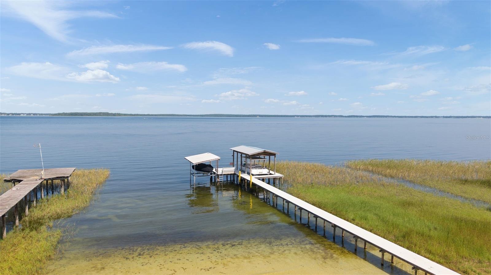 Make sure to check out the fly over video and the 360 degree tour and check out the WOOD PLANK ceiling in the main living room!! Why spend hours driving to the beach when the beach is your backyard? Welcome to your own slice of paradise on beautiful Lake Weir, where every day feels like a vacation. Fall asleep to breathtaking sunsets over the water, spend your afternoons swimming from your private sandy shoreline, boating, water skiing, fishing, paddleboarding, or simply relaxing on the dock while soaking in unforgettable sunsets.
Designed for entertaining and making lifelong memories, the main home offers an open floor plan with soaring vaulted ceilings, a stunning fireplace, and expansive windows that frame spectacular lake views. The beautifully updated kitchen features Schueler maple cabinetry, Silestone countertops, a center island, breakfast bar, and flows seamlessly into the spacious dining area and great room. Just outside, a two-level deck overlooks the lake, creating the perfect setting for morning coffee, evening cocktails, or hosting family and friends after a day on the water.
Need room for everyone? The home features three bedrooms on the main level plus a spacious loft with its own half bath, making it easy to accommodate large gatherings, weekend guests, or holiday celebrations.
Lake life is effortless with your private pier, a recently rebuilt 100-foot WearDeck dock backed by a lifetime warranty, ready for all your water toys. After a swim, rinse off in the outdoor shower before settling in for another relaxing evening by the lake.
The property is surrounded by magnificent mature live oak trees that provide incredible shade and create a peaceful, park-like setting. 
This home has also been thoughtfully updated for efficiency and peace of mind with owner-owned solar panels that dramatically reduce electric costs, A BRAND NEW ROOF JULY 2026 a new HVAC system (2025), fresh exterior paint (2023), new gutters (2022), a whole-house water filtration system, updated well pump and piping, underground electric service, backup generator, irrigation system, and more.
Convenience is never far away. You're only about a mile from everyday essentials including a gas station, hardware store, convenience store, and neighborhood grocery, while just minutes from The Villages where you'll enjoy nightly entertainment, championship golf, shopping, dining, and countless activities.
If you've been dreaming about the lakefront lifestyle, this is your opportunity to enjoy all the fun without the crowds, traffic, or expense of coastal living. Launch the boat whenever you want, fish from your own dock, swim from your own sandy beach, and create memories that last a lifetime—all from the comfort of your own backyard.
Property Highlights
• Private sandy beach on Lake Weir
• Private pier with recently rebuilt 100-foot WearDeck dock
• Three bedrooms plus loft with half bath
• Vaulted great room with fireplace
• Updated kitchen with Schueler maple cabinetry, Silestone countertops, island, and breakfast bar
• Spacious dining area overlooking the lake
• Florida room with Mexican pavers
• Built-in wet bar
• Plantation shutters
• Two-level lakeside deck
• Outdoor shower
• Attached two-car garage
• Whole-house water filtration system
• Owner-owned solar panels
• Backup generator
• Underground electric service
• Irrigation system