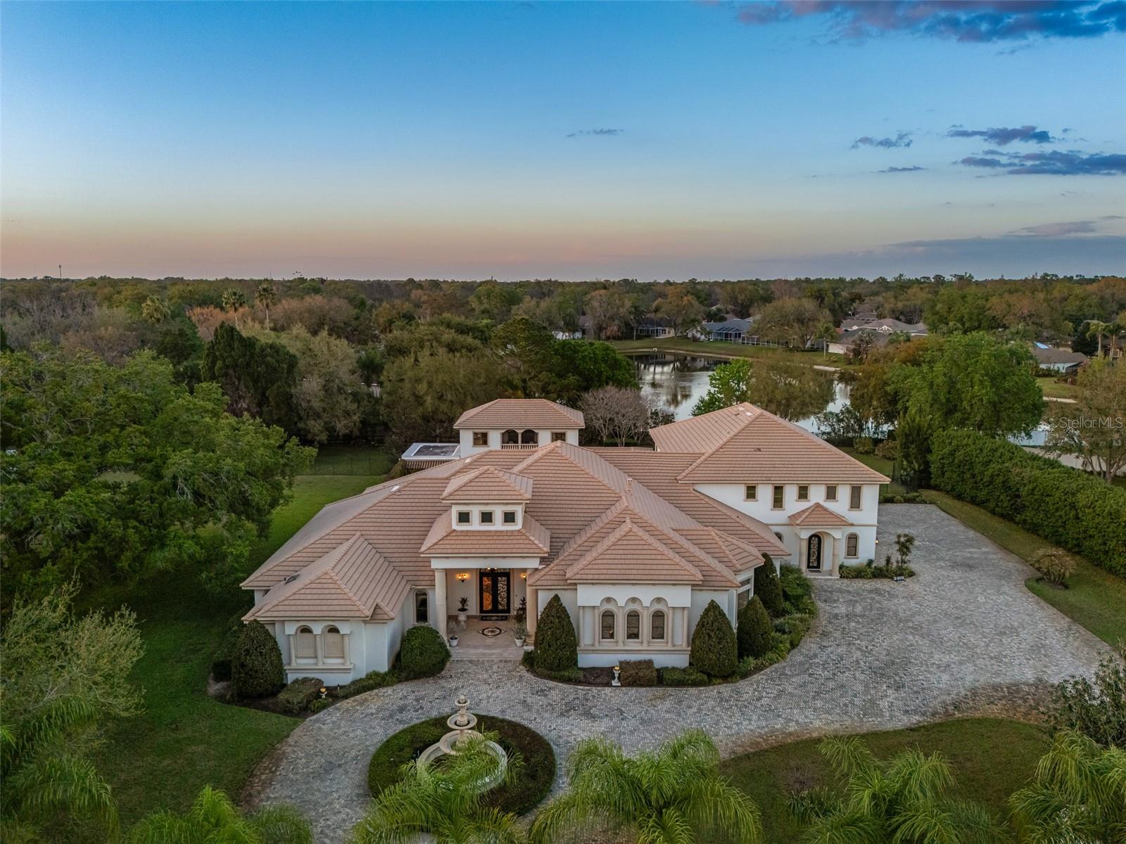 Under contract-accepting backup offers. Extraordinary luxury residence situated over 1.4 beautiful acres, offering privacy and discretion, and positioned on a scenic pond. This one-of-one, Mediterranean masterpiece, greets you with a gated, circular driveway centered around a magnificent fountain while offering an astounding floor plan that features a detached guest house, and can be available fully furnished. The interior radiates sophistication, beginning in the grand double door entrance, soaring coffered ceilings throughout the living area, complemented by architectural excellence around every corner, a stunning cast stone double-sided fireplace and endless detailed millwork throughout. A key focal point of this estate is a chef’s culinary dream, featuring a considerable center island anchored by a striking light fixture. This high-end kitchen is equipped for grand-scale entertaining with a 48” Wolf cooktop, a 6-foot GE Monogram hidden panel refrigerator, dual built-in ovens, two dishwashers and a separate pantry room, with glass cabinets and a huge island. The living spaces flow seamlessly, offering multiple gathering and conversation areas, accented by a chic grand piano, formal dining room and a hidden powder bath. Retreat to ultimate privacy with five spacious bedrooms, including two first-level, primary suites both with oversized walk-in showers, deep soaking tubs and multiple built out closets. A grand staircase or elevator will guide the path to the upstairs entertainment area featuring the media room, fitness area/game room flex space, and two additional bedrooms. A separate guest house apartment with private access offers a full kitchen, living room, bedroom, bath and balcony over the courtyard as a secluded haven for visitors. For the automotive enthusiast, an oversized four-car garage gives ample space along with a dedicated storage room within the garage. The estate transforms into a personal resort within the travertine courtyard, featuring a heated pool, spillover spa, and multiple areas for gathering and entertaining. This outdoor space is unmatched, boasting a covered summer kitchen with bistro seating, alongside a separate bar countertop, and two covered areas offering an outdoor fireplace or tv viewing and lots of storage. This scenic space is adjacent to the spacious grass backyard, all of which is fenced and ideal for yard games or pets to play freely. Between Tampa and Lakeland, this residence combines the charm of historic Plant City with the privacy and luxury details of an outstanding estate.