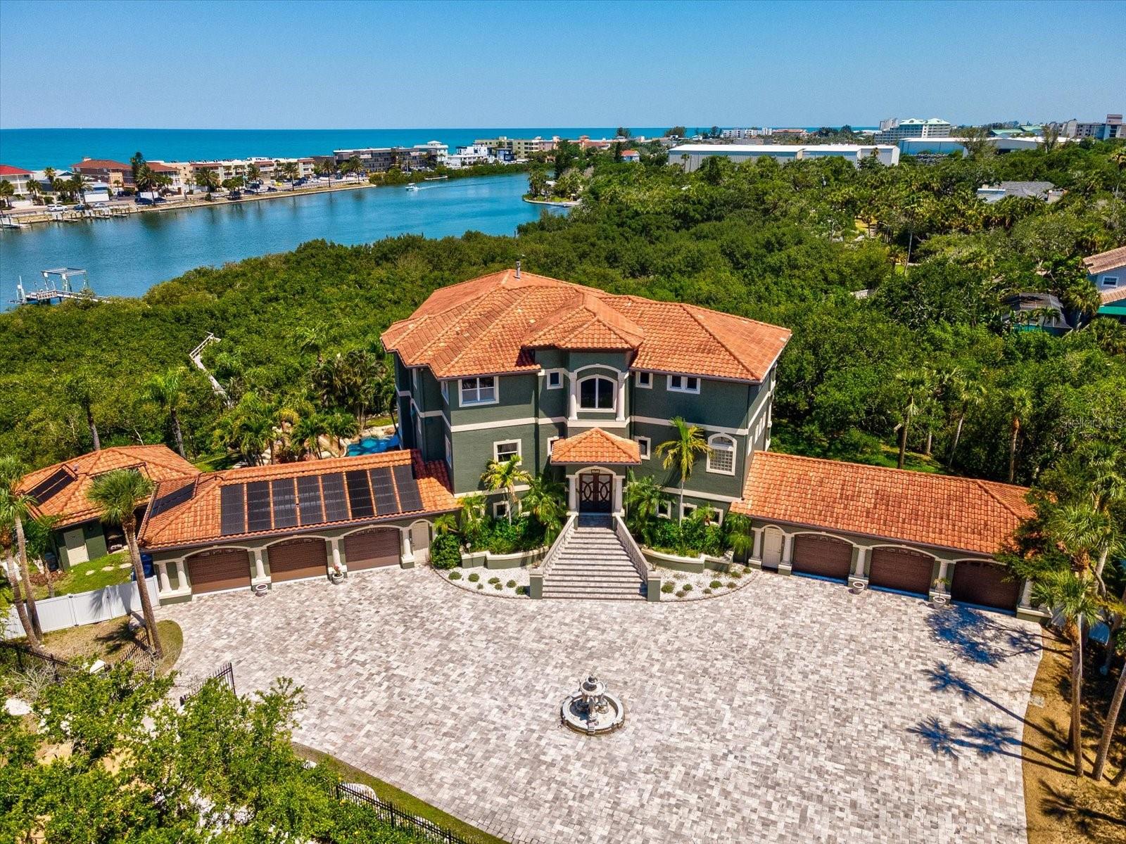 An extraordinary waterfront estate set on 2.75 private acres, this grand residence offers an impressive 9,136 square feet of luxurious living space designed for both lavish entertaining and everyday comfort. Completely fenced and gated with separate entrance and exit access, the property features a private pavered road, expansive driveway with ample RV and boat parking, and a remarkable 6-car garage with enough ceiling clearance to accommodate vehicle lifts for up to 12 cars total. Surrounded by lush tropical landscaping with no direct neighbors, the outdoor oasis showcases a custom lagoon-style pool complete with a jacuzzi, slide, walk-in entry, multiple sun shelves, and dual waterfalls, along with a spacious cabana, private dock with two lifts, whole-home generator, and 1,000-gallon propane tank. An elevator services all three floors for seamless convenience. The first level was designed with entertaining in mind, featuring two walls of paneled sliders that create a true indoor-outdoor experience overlooking the pool and spa. Highlights include a 300-bottle temperature-controlled walk-in wine cellar, theatre room with upgraded AV equipment and wet bar, expansive gathering spaces ideal for billiards or poker, oversized island seating for 10, and an impressive lounge area. A private in-law suite with separate entrance offers a full bath, large flex space, kitchenette, and full-size refrigerator. The second floor serves as the heart of the home with a newly renovated chef’s kitchen outfitted with high-end Thermador appliances, double ovens, two oversized islands, breakfast nook, and a large walk-in butler’s pantry. The kitchen overlooks a cozy sitting area with fireplace and opens to a spacious terrace with outdoor grill. Also on this level are a stunning office with coffered ceilings, private bath, and balcony access, formal dining room, and a large guest suite with en-suite bath and private terrace. The third floor offers three additional en-suite bedrooms plus a large bonus room that can easily function as a fourth bedroom. The primary suite is truly exceptional, featuring a wraparound terrace with panoramic intracoastal and Gulf views, wet bar, double-sided fireplace, dual walk-in closets, dual vanities, and an oversized walk-in shower with four shower heads. Additional upgrades include a Control4 smart home system, surround sound throughout, and custom interior and exterior lighting. This exceptional waterfront retreat remained high and dry through recent storms, offering peace of mind alongside unparalleled luxury living.