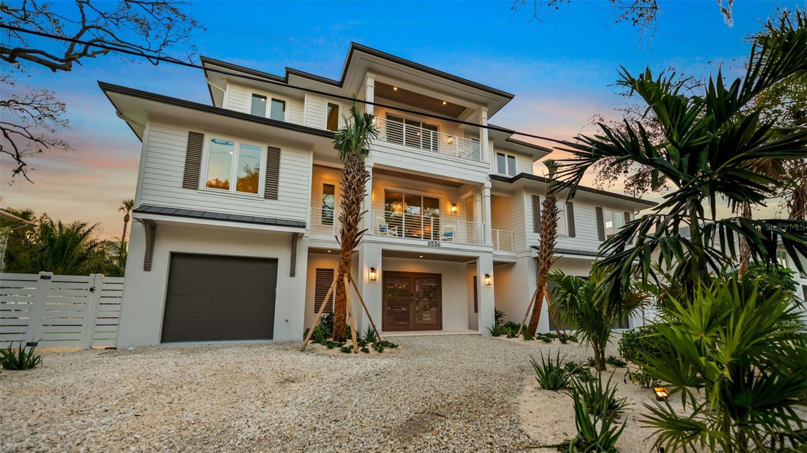 There is only one — Siesta Sun Sets. Set against the quiet backdrop of Sabal Lake, with glimpses of the Gulf beyond, this residence unfolds with a sense of irresistible intention. Influenced by West Indies architecture, the design blends expansive indoor-outdoor living with natural textures, layered spaces, and a palette that mirrors its surroundings — soothing, sun-washed, and enduring. Across more than 4,000 square feet, the home offers seven incredible en-suite bedrooms and multiple living areas designed for both gathering and restful retreat. The great room anchors the experience, where kitchen, dining, and living spaces open outward to twin balconies — one overlooking the extensive grounds, the other framed by mature oaks, offering a quiet contrast of shade and light. Above, a private club level introduces a more intimate setting — a theater-style lounge, additional suites, and access to the rooftop deck. It is here, at the highest point of the home, that the name reveals itself. As day transitions to evening and the Gulf reflects gold, the softening sky reveals stunning sunsets,  becoming the backdrop against which you count your blessings. Below, the grounds are equally considered. A multi-sport court — rare in both scale and versatility — sits alongside a resort-style pool and 360-degree spillover spa, creating a setting as seductive as it is serene. Covered outdoor living spaces extend the home’s presence, offering multiple areas for dining, gathering, and quiet retreat, all within a private, fully enclosed landscape. Siesta Sun Sets is not defined by any one feature, but by the way it brings them together — water, light, elevation, and space — into a residence that feels both grounded and removed, exclusive and secluded.  A masterwork of resilient engineering and high-end coastal construction, this estate is architecturally primed to withstand coastal elements while serving as a premier venue for grand-scale entertaining and lucrative seasonal retreats. More than a home, Siesta Sun Sets is part of an exclusive Vunique collection with a proven history of strong rental performance — each residence one-of-one, purpose-built to balance bold design and bespoke experience. Here, ownership transcends address; it becomes a mark of belonging to something beautifully uncommon.