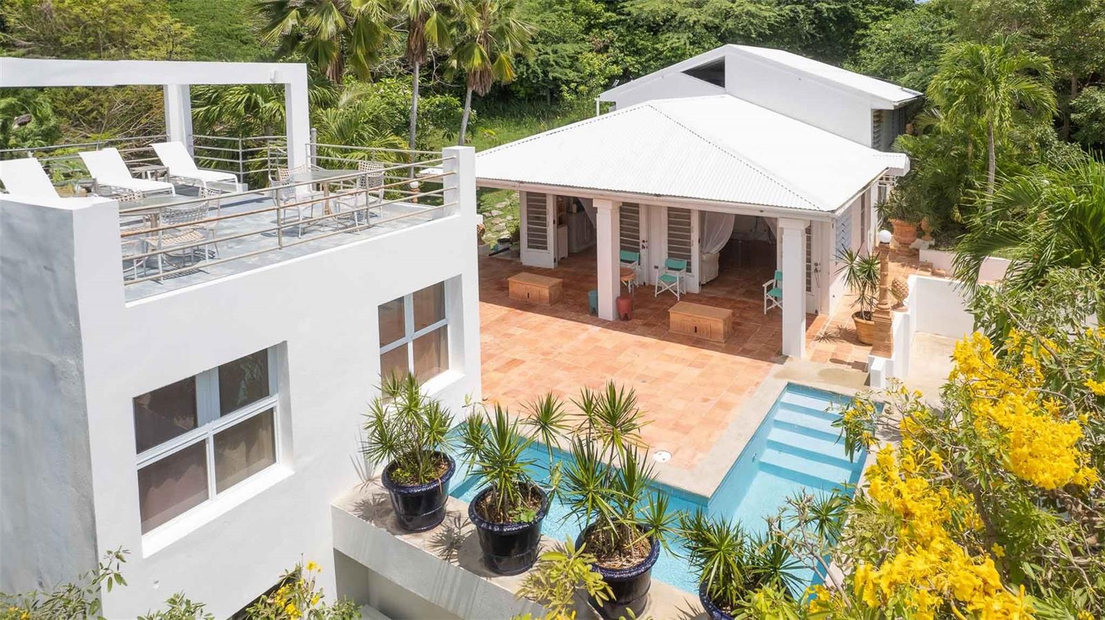 La Serenísima is a rare and timeless property located on a private cul-de-sac in the desirable Bravos de Boston neighborhood of Vieques. Designed with Caribbean sensibility and built in 1993 by the respected firm Cristofol, Hernández-Dupuy, this custom home sits on a lush, one-acre parcel of fully fenced land surrounded by mature gardens and tropical trees that provide exceptional privacy.

The property features two structures connected by an outdoor living area and L-shaped marmolite pool. The main residence includes a vaulted living room with exposed beams and terracotta Saltillo tile floors that continue throughout the home and patio areas. French doors open to the pool terrace, capturing trade winds and maximizing cross-ventilation.

Upstairs are two spacious bedrooms, each with air conditioning and a dedicated bathroom. The primary suite includes both an interior bath and a private outdoor courtyard shower. The open-concept kitchen features soaring 21-foot ceilings, built-in shelving, and generous counter space, offering both elegance and function.

The second structure is a self-contained studio with a kitchen, bathroom, and private rooftop sundeck accessed by a spiral staircase. Below the studio is an enclosed flex space ideal for storage, a workshop, or future creative use.

The pool area, surrounded by natural landscaping, is designed for relaxing or entertaining. At 4 feet deep and 5 feet wide with built-in steps, it offers a refreshing spot to cool off under the Caribbean sun.

The acre of land is sloped and usable, offering a rare combination of privacy and possibility. There is ample room for expansion—whether through the addition of guest casitas, recreational amenities, or further gardens—yet the existing mature landscaping already creates a natural buffer from neighboring properties and street noise.

Every room in the home is designed to interact with the outdoor environment, emphasizing indoor-outdoor living. The home has never been used as a rental and has been meticulously cared for by its original owners.

With three bedrooms, three bathrooms, two kitchens, multiple living areas, and outdoor amenities including a pool, patios, and rooftop deck, this property offers both comfort and flexibility. It is well suited as a primary residence, seasonal home, or multigenerational retreat.

Located centrally on the island, this Bravos de Boston property offers easy access to both beaches and town amenities while feeling like a secluded retreat.

This is a thoughtfully designed and well-constructed home that balances craftsmanship, natural beauty, and modern convenience—an exceptional opportunity on the island of Vieques.