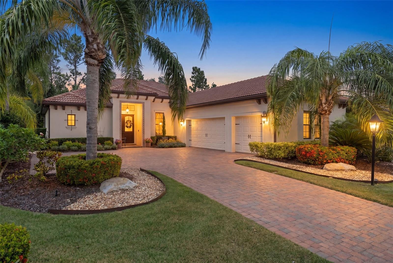 Welcome to this beautifully designed John Cannon home located behind the gates of Country Club East. Situated within one of the area’s most desirable communities offering two private clubhouses and exceptional amenities, this thoughtfully appointed split floor plan residence features 4 bedrooms, 3 baths, a dedicated office, and wet bar perfectly blending comfort, style, and functionality throughout. From the moment you arrive, the paver driveway, tropical landscaping, and Mediterranean-style tile roof create a warm and inviting first impression. Inside, handcrafted double entry doors open to high ceilings and a spacious open-concept layout filled with natural light. Rich luxury vinyl flooring and ceramic tile carry throughout the main living areas, creating a timeless and cohesive feel. The kitchen is both stylish and practical, featuring custom white cabinetry, granite countertops, and premium Jenn-Air appliances. A faux stucco painted copper range hood adds character above the gas cooktop, while the oversized island with a copper undermount sink serves as the heart of the home. Nearby, the teal wet bar adds a bold designer touch complete with a wine cooler and additional entertaining space perfect for hosting guests. Designed with privacy in mind, the split floor plan offers a secluded primary suite separate from the guest accommodations, creating a comfortable retreat for both homeowners and visitors alike. The living room opens through sliding glass doors to the screened lanai, where indoor and outdoor living come together seamlessly. The salt water pool and spa are accented with decorative tile, a fountain feature, and lush tropical landscaping for added privacy. A gas outdoor fireplace creates the perfect setting for relaxing evenings, while both the primary suite and second guest bedroom offer direct access to the lanai. For added peace of mind, the home is equipped with a generator, offering additional convenience and preparedness throughout the year.