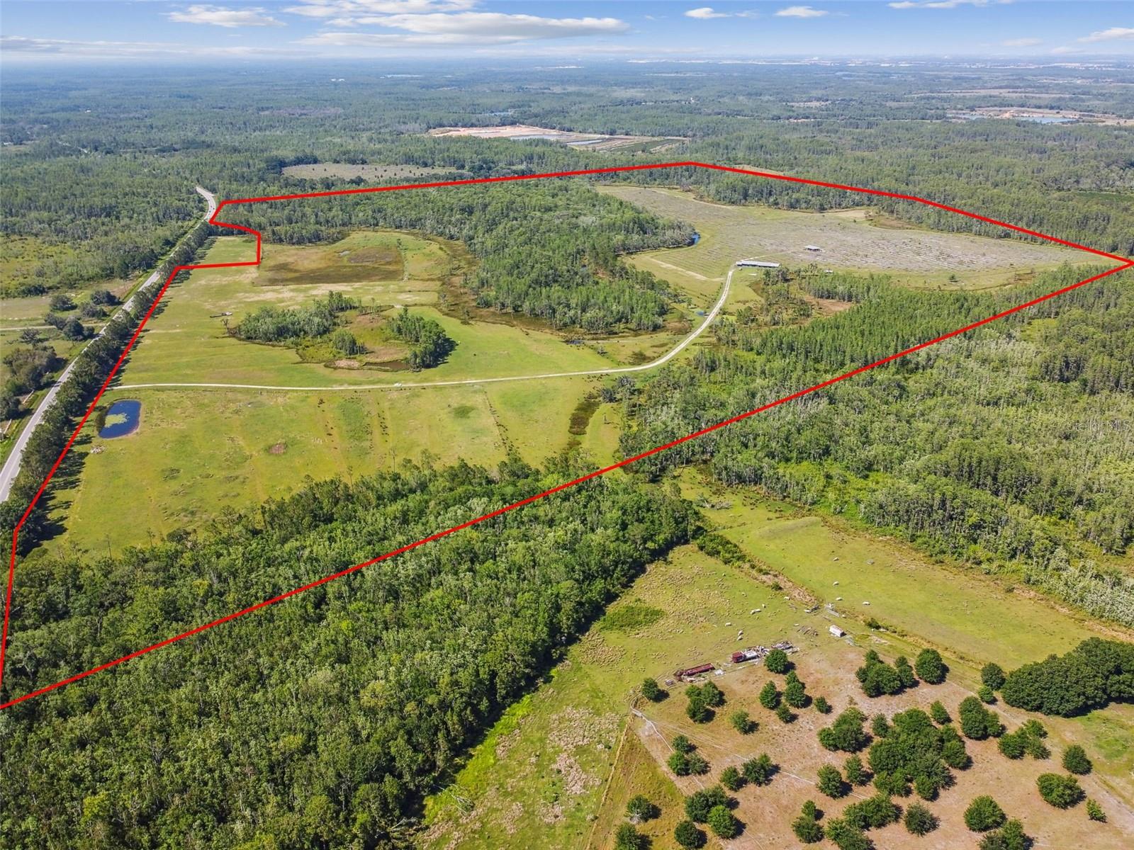 The St Rd 557 Lake Alfred property (Parcel ID: 262708000000012010) spans 305 acres, with approximately 92 acres of developable land & is strategically located just 45 minutes (39.6 miles) from Orlando International Airport and 38 minutes (27.3 miles) from Walt Disney World. Currently zoned for agriculture at one dwelling unit per five acres, the site yields about 20 lots, but its contiguity to the City of Lake Alfred offers a strong opportunity for annexation, unlocking access to city water and sewer and enabling rezoning to a much higher density. With a Village Residential designation allowing four units per acre, the property has a projected yield of roughly 408 units. Directly across SR 557, Meritage Homes’ Silver Lakes community has already extended water & sewer infrastructure to their entrance, enhancing feasibility for development. CR 557 is scheduled to be widened to four lanes beginning in summer 2025, with completion expected in three years, and a roundabout will be added at the intersection of CR 557A and CR 557 to improve traffic flow. A five-acre retention pond adjacent to CR 557 will slightly reduce the total developable acreage. The property sits within an active development corridor with major builders such as Pulte, DR Horton, Meritage, and American Homes driving growth, and additional utility extensions by nearby projects will further support development. While the site benefits from strong accessibility and regional demand, considerations include its location within a 100-year flood zone requiring fill and flood insurance, areas of poorly drained soil, and an irregular parcel shape that may constrain layout and reduce final lot yield. Entitlement approvals for annexation, land use amendment, and rezoning are required, but all have a high probability of success and can be pursued concurrently, with an estimated approval timeline of six to twelve months.
Directions: From I-4, take exit 44 toward Polk City. Turn L onto SR 559, R on CR 557.