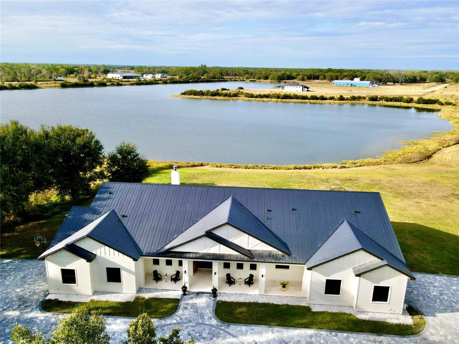 Welcome to an extraordinary 2025 luxury modern farmhouse estate, offering 3,591 square feet of refined heated living space and 5,595 total square feet of thoughtfully crafted design. Set on an expansive, seaplane-friendly lakefront property, this residence blends modern elegance with timeless farmhouse character to create a lifestyle of comfort, sophistication, and privacy.
A striking aluminum roof and an impressive 50-foot covered front porch set the tone upon arrival. Inside, soaring 12-foot ceilings and a dramatic 14-foot cathedral ceiling over the living room and kitchen create an expansive, light-filled atmosphere. Custom hardwood floors, premium stone selections, and meticulous craftsmanship elevate every inch of the interior.
The chef’s kitchen is a true centerpiece of the home, curated for both beauty and performance. It features premium appliances, including a 48-inch gas range with hood and pot filler, a Sub-Zero refrigerator and freezer, and a dedicated hot beverage station. Solid wood cabinetry is enhanced with soft LED accent lighting at the kick plates and beneath the upper cabinets, adding a warm and luxurious glow. A spacious walk-through pantry with its own sink provides added convenience and exceptional functionality.
The estate offers four well-appointed bedrooms, five full baths, a private study or den, and a large bonus/play area ideally situated near the secondary bedrooms—perfect for families or guests. A multi-zoned air-conditioning system ensures personalized comfort throughout the home.
The primary bedroom retreat is a sanctuary of style and serenity, featuring an ensuite adorned with expansive stonework, a built-in makeup vanity, and a standalone soaking tub positioned to overlook the surrounding woods. An expansive walk-in closet completes this luxurious space.
The outdoor living experience is truly exceptional. A stunning lanai features a real wood-burning fireplace and overlooks a fully automated heated pool and spa. A newly constructed black aluminum fence around the perimeter of the pool deck has recently been installed and updated photos are pending. Beyond the pool lies approximately 500 feet of deeded water frontage along a breathtaking, considerably deep estimated 40' deep 30-acre lake. This rare body of water is ideal not only for boating, jet skis, and fishing but is also perfectly suited for seaplane access. You can build your own private dock and enjoy the unparalleled beauty and freedom of true lakefront living.
The estate includes two separate garages: a traditional two-car garage and an oversized one-car garage ideal for storing tools, machinery, or ATV’s to run the property with. Horses are welcome, offering even greater versatility and lifestyle options.
A rare and unique benefit of this location is its just 14 miles to the Wauchula Municipal Airport, a low-volume airport which serves mostly the needs of private and recreational aviation. An exceptional feature for aviation enthusiasts seeking convenient, private access. 
Despite the tranquil setting, the home remains only 20 minutes from the Lakewood Ranch area for grocery stores, dining, and conveniences. Bradenton is roughly 35 minutes away, Sarasota approximately 40 minutes, and Anna Maria Island’s world-class Gulf beaches just 50 to 55 minutes from your doorstep.