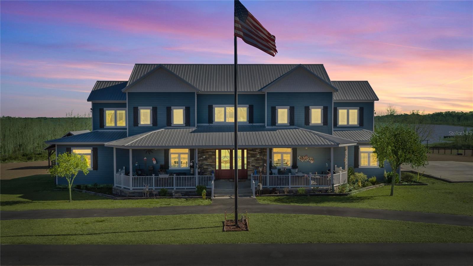 Experience extraordinary lakefront living on this breathtaking waterfront farmhouse estate, privately set on almost 20 acres beneath a canopy of mature oaks with sweeping water views, equestrian amenities, and wide-open acreage. Designed for both luxury and functionality, this exceptional property offers over 5,500 square feet in the main residence, a detached two-story guest apartment, multiple garages, resort-style outdoor living, and a beautifully designed barn setup ideal for horses, livestock, storage, or future expansion.
The striking main home showcases a classic metal roof, crisp coastal-inspired exterior, and expansive wraparound porches overlooking the lake. Inside, soaring ceilings, wood-look tile flooring, and sun-filled living spaces create an inviting yet dramatic atmosphere. The great room flows seamlessly into the chef’s kitchen featuring custom cabinetry, granite countertops, a large center island with farmhouse sink, gas cooktop, double ovens, bar seating, and a massive walk-in pantry. Oversized dining windows perfectly frame the picturesque lake views.
The main residence offers four bedrooms and four-and-a-half baths, including two owner’s suites. The primary suite on the main level overlooks the water and features a spa-inspired bath complete with a clawfoot soaking tub, dual rain showers, double vanities, and an expansive walk-in closet. Additional interior highlights include a private office with French doors and custom built-ins, a dedicated movie room, and an oversized laundry room with a Murphy bed, utility sink, and abundant storage. Upstairs, a loft overlooks the main living area and entryway and is accompanied by two additional bedrooms, including one with an oversized bath and walk-in closet and another with a private bath and adjoining game room.
Outdoor living is equally impressive with a lakeside pavilion featuring a hot tub, outdoor kitchen with butcher block countertops, gas grill, wood-burning fireplace, and TV. A private sandy beach and dock with gazebo create the perfect setting for boating, fishing, or relaxing at sunset.
Equestrian and acreage amenities are thoughtfully designed for both everyday functionality and future flexibility. The barn currently offers four stalls with room to easily add four more, along with a climate-controlled tack room featuring a full bath, utility sink, water fountain, and ice maker. Additional improvements include an outdoor wash rack with cross ties and concrete flooring, covered trailer parking, a spacious three-bay pole barn, three paddocks, and two expansive pastures that could easily be converted into additional paddocks, a riding arena, or recreational space.
Car enthusiasts and hobbyists will appreciate the impressive five-bay garage complete with a two-bedroom, one-and-a-half-bath apartment, as well as an additional three-bay garage offering exceptional storage and versatility.
A rare opportunity to own a secluded waterfront retreat that seamlessly combines luxury living, resort-style outdoor spaces, equestrian functionality, and endless possibilities for a private estate, hobby farm, or active outdoor lifestyle.