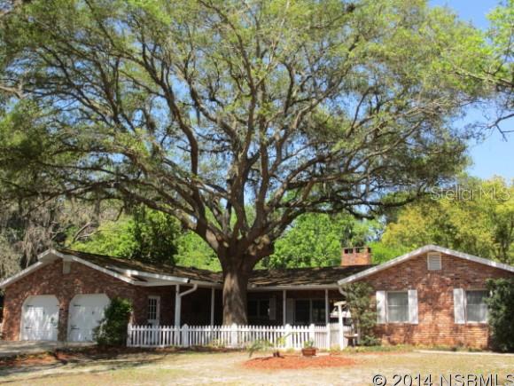 Nestled under the oaks this sprawling 4-5 bedroom home offers endless possibilities. Country living at it's finest just a short drive to upscale shopping, eateries, medical facilities, highways and to the beach! Situated on over 3+ acres this Old World brick home has many unique features including Pine Wood flooring, exposed brick accent walls, wood beams, fireplace, skylights and large open gathering areas. Kitchen has large center island with prep sink, tiled counters & beautiful brick hearth style cooking area featuring a Jennaire cooktop. Master bedroom has tiled flooring and updated bath & dressing area. Secondary bedrooms are ample in size with plenty of closet space. 4th bedroom has ensuite bath and would make a perfect inlaw/teen or extended family living area. 5th bedroom could easily be an in home office. Other inside features include security system, brick pavered foyer, & inside laundry. French doors lead to screened porch overlooking sparkling blue pool and patio area. Main home has a 2 car oversize attached garage. Exterior features a fabulous detached outbuilding w/soaring ceilings which can accommodate all the toys including an RV garage space, boat parking, or workshop. It is attached to a concrete block 4 stall barn with inside & outside stalls and tack room. Totally fenced pasture for horses. Back of property is adjacent to Spruce Creek. Looking for a multiple use property then put this one on your list.