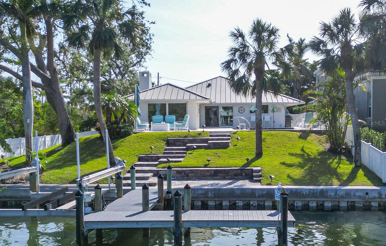 Discover the ultimate blend of coastal elegance and modern design in this fully remodeled 3 bedroom, 3 bathroom home located just steps from the sandy shores of Lido Beach and the world-famous St. Armand’s Circle. Imagine morning strolls on the beach, afternoons exploring boutique shops, and evenings savoring fine dining, all within walking distance from your doorstep. A home designed for effortless living, step inside this elevated 2,600 square foot retreat and be greeted by a light-filled, open concept floor plan that invites comfort and style. The professionally designed interiors feature a chef’s kitchen with Thermador appliances, a large island, and cozy eat in area perfect for gatherings. The primary suite is a sanctuary in itself, boasting an oversized walk-in-closet and spa-inspired bathroom. Two additional bedrooms share a beautifully updated guest bath, ensuring space and privacy for all. The thoughtful design extends outdoors to a brand new Travertine lanai showcasing a heated pool and spa, surrounded by an expansive terrace and stunning canal views. There is also a gas fire pit where you can enjoy our world famous sunsets! Watch dolphins, manatees, and fish glide through the water from your private dock with a 66 foot newly capped seawall and 4,000 pound boat lift – a boater’s paradise. Move in ready, with peace of mind as this home is packed with modern upgrades including updated mechanical systems, on demand hot water tank, hurricane-rated sliders and windows, a durable metal roof with new gutters, storm rated garage door with ac system, and a new front walkway and driveway with a sprinkler system. Best of all, this home sustained no damage from recent storms.  Property is a quick drive to downtown Sarasota, fine dining, entertainment, and the International Sarasota Airport. The property is offered fully furnished with high end pieces, making your move seamless. Don’t miss this rare opportunity. Whether you’re seeking a permanent residence or a vacation retreat, this coastal contemporary gem delivers it all.