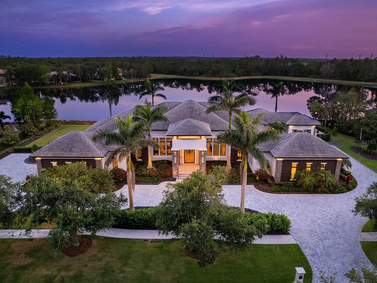 This architectural masterpiece by John Cannon Homes, in The Concession, is a stunning blend of high design and modern functionality. A circular driveway and immaculate landscaping create a grand impression. At the same time, the preserve across the street and behind the house offers permanent privacy—a one-of-a-kind property. The large stone columns and the impressive glass pivot door highlight the home's elegant craftsmanship. As you enter the foyer, a breathtaking lake view unfolds through the large glass sliders, showcasing the expansive, endless pool. Elegant wood-look tile flooring flows throughout the home, complemented by impact glass, remote-controlled blinds, custom draperies, designer lighting and gold-accented hardware. The great room is sleek and spacious and embodies luxurious comfort, highlighted by a dramatic coffered ceiling and a media wall featuring built-in shelving, a backlit agate mantle, a linear 120-inch fireplace and a 100-inch television. Adjacent niches are perfect for wine tastings or intimate gatherings. At the heart of the home, the gourmet kitchen impresses with an oversized floating island wrapped in waterfall-edge quartz counters and striking pendant lights cascading from a custom dropped ceiling. Premium appliances include a Sub-Zero refrigerator, Dacor induction cooktop, Fisher & Paykel double dishwashing drawers, and a stylish dry bar nearby. The prep kitchen's huge windows view the garden and add culinary versatility, with a Viking gas range, True refrigerator, Viking dishwasher and a large walk-in pantry. The remarkable primary wing encompasses the entire left side of the house. It is entered through solid-core double doors and features a versatile coffee bar, spacious sitting area, private lanai access, dual custom closets, an in-closet vanity and private office. The spa-like primary bath offers dual vanities, a freestanding tub, an oversized walk-in shower with multiple showerheads, Kohler® fixtures and a secluded courtyard. Two expansive walk-in closets provide custom storage. The VIP suite lives like a second primary—complete with a private wet bar, pool access via sliding doors, a spa-style bath and a wood-accented lighted wall that continues along the ceiling. All guest bedrooms include en-suite baths and walk-in closets. A stylish powder bath, a versatile bonus suite and a well-appointed media room complete the interior living spaces. The outdoor oasis provides an extraordinary design. A fully equipped outdoor kitchen boasts dolomite countertops, an accent wall, custom lighting, a premium Lynx grill, sink and two Perlick beverage drawers. The Pebble-Tec saltwater infinity pool is framed by dramatic fire and water features, a raised spa, and a panoramic screen enclosure that captures the lakefront setting. A custom-designed 75-inch screen is hidden in the ceiling and effortlessly drops down for viewing from any angle. A porcelain lanai on concrete deck with hidden drains, integrated landscape speakers, and lush, professionally designed landscaping. Additional upgrade features include two tankless water heaters, a climate-controlled storage room, hidden HVAC vents and two oversized two-car garages, one with ceiling height to accommodate a lift and more. Home automation allows for effortless control of lighting, audio and security.