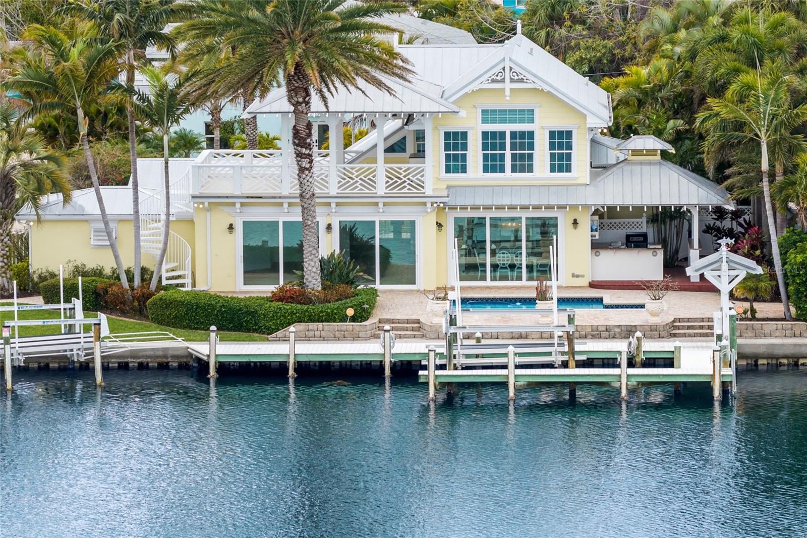 One or more photo(s) has been virtually staged. Spectacular Waterfront Key West-Style Home on Bimini Bay!!  This beautifully maintained 4 bedroom, 3 bathroom single-family home, offering 2,775 sq ft of living space on a spacious 9,400 sq ft lot.  Meticulously crafted with thoughtful architecture, interiors and landscaping by legendary award-winning architect, Emily Anne Smith. 
As you step in, you’ll notice the double height ceilings, unique, blue glass chandelier in the entry that leads into the spacious open floor plan.  Large slider impact doors that create natural light and provide stunning views of Bimini bay.  The living room is warmed by a modern linear fireplace complemented by a wall of custom illuminated floating shelves and built-in cabinetry with an exquisite backlit blue agate Antolini countertop.  A chef's dream, the kitchen is equipped with Monogram Professional Series appliances, quartz countertops and a thoughtful layout. Abutting the kitchen is the large laundry room leading to an oversized two car garage.   A first floor primary suite has privacy and features an oversized en suite bathroom with double marble vanity.  In addition, the first floor has a full bathroom with a frameless glass shower, custom blue glass waterfall sink and two generously sized bedrooms.  The entire second level luxurious main suite features breathtaking water views, cathedral ceilings, dual custom walk-in closets, a large spa-like bathroom with a freestanding jetted tub surrounded by backlit quarzite counters, Bisazza tile, modern crystal chandelier, dual Carrara marble vanities, and spacious modern reclaimed wood porcelain tile walk-in shower. An expansive rooftop terrace and gazebo, not to be missed, offers a stunning 360-degree view of Anna Maria Island.  Step outside to entertain on the expansive pool deck with a large pool, or retreat to the private upper deck for quiet sunsets and bay breezes.  Resort style outdoor area includes an outdoor kitchen and bar, outdoor shower, covered fishing station, dual lift and dock area for jet skis and ample space to accommodate a large yacht, fishing or sport boat, making indoor/outdoor living and entertaining flawless.  Brand new Interior and exterior paint throughout!  Enjoy deep-water frontage with no bridges to the Gulf of Mexico and your own 9,000 lb boat lift — perfect for boating enthusiasts who want effortless Gulf access and quick runs to the open water. 
The home is just a short golf cart ride gorgeous sand beaches, making it ideal for beach lovers, families, or those seeking the ultimate Florida island lifestyle.