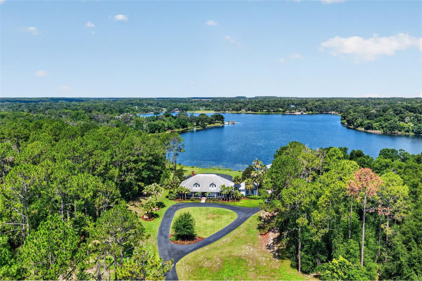 Discover an extraordinary lakefront estate offering 11.25 private acres, a private boathouse, and direct frontage on the pristine waters of Lake Seneca. Surrounded by majestic mature trees, this remarkable property provides the perfect blend of luxury, privacy, and natural beauty. A sweeping circular driveway leads to the elegant residence, where lush landscaping, ornamental palms, a side-entry oversized garage, and a welcoming front porch create an unforgettable first impression. Inside, refined rustic elegance defines every space. The grand foyer showcases warm natural light, rich wood accents, beadboard walls and ceilings, custom millwork, and a stunning handcrafted staircase that immediately sets the tone for the home's timeless character. The front living room offers peaceful views of the manicured grounds and provides flexible space for a formal sitting room, library, or dining room. The heart of the home is the spectacular family room, where soaring vaulted ceilings, pecky cypress walls, oversized windows, and glass sliders frame breathtaking panoramic views of Lake Seneca. A dramatic floor-to-ceiling stone fireplace serves as the centerpiece, creating the perfect gathering place for family and guests. Designed with both beauty and function in mind, the custom chef's kitchen features abundant handcrafted cabinetry, black stone countertops, stainless steel appliances, dual wall ovens, a spacious prep island with an oversized sink and seating, a walk-in pantry, and a cozy dining alcove overlooking the pool and lake. The showpiece is the commercial-grade 8-burner Viking propane range with a professional stainless-steel hood. Entertaining is effortless as the living spaces extend seamlessly onto the expansive screened lanai. Finished with paver flooring, generous covered seating areas, and a sparkling pool overlooking the lake, this outdoor retreat offers the perfect setting for relaxing or hosting unforgettable gatherings while enjoying tranquil water views and refreshing breezes. The main level also includes a full guest bath, a spacious laundry and storage room that could easily function as a butler's pantry, plus the added security of a whole-house generator and a 500-gallon propane tank. The primary suite is a peaceful sanctuary featuring hardwood floors, plantation shutters, private access to the lanai, beautiful pool and lake views, a walk-in closet, and an en-suite bath with natural stone finishes and an oversized walk-in shower. Upstairs, you'll find two generously sized guest suites, each with its own private bathroom. A massive climate-controlled storage room offers exceptional space for seasonal décor and collectibles, while a bright windowed alcove creates the perfect spot for a home gym, reading nook, or office. Outside, the possibilities are endless. Spend your days lounging poolside, strolling through your private wooded acreage, fishing from your dock, entertaining on the boathouse sun deck, or exploring Lake Seneca by boat, paddleboard, or kayak. Offering unmatched privacy while remaining just minutes from shopping, dining, and major roadways, this exceptional waterfront estate delivers the very best of Florida luxury living. Experience the beauty, serenity, and lifestyle that only true lakefront living can provide.