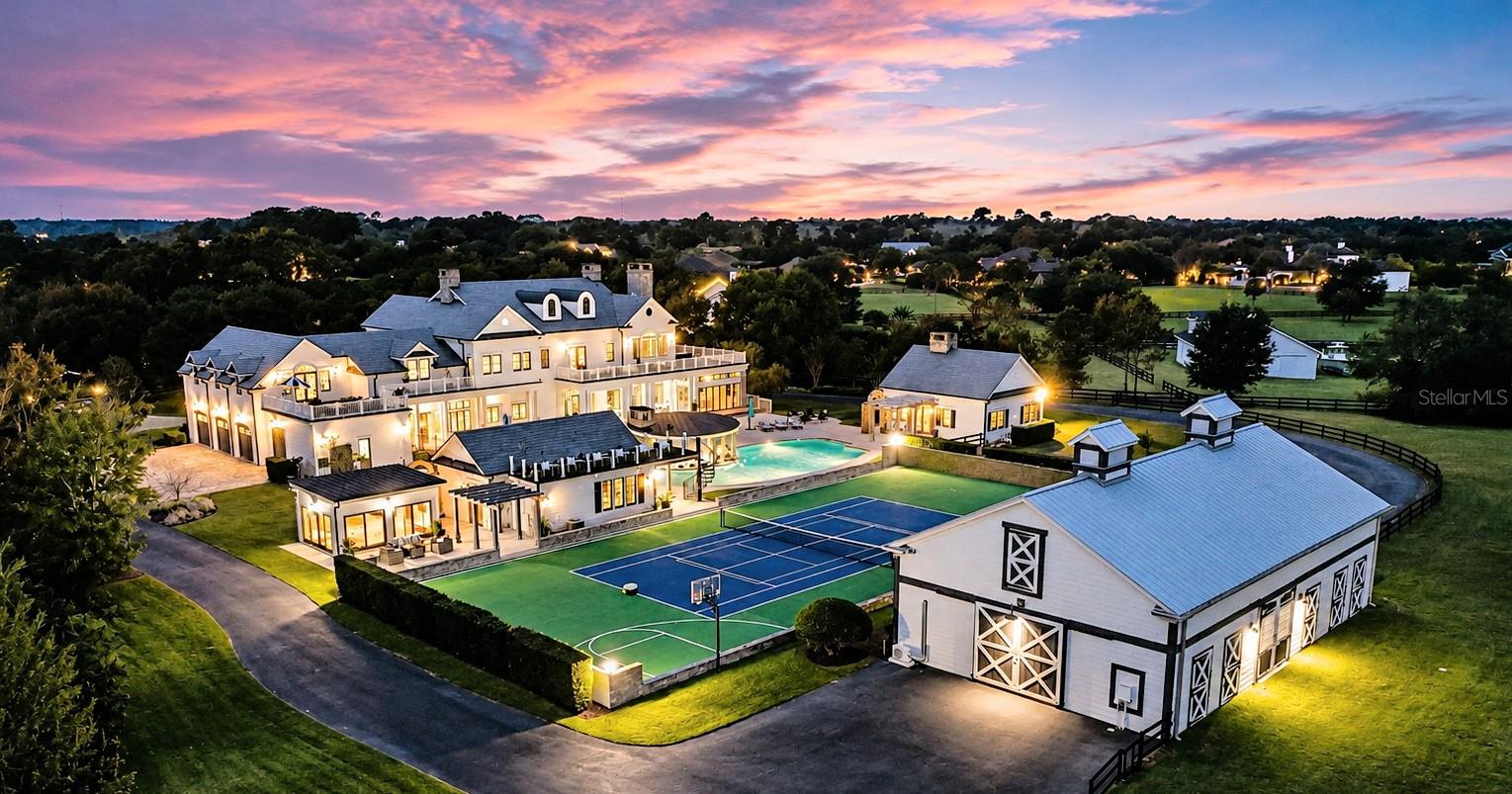 What if your home could replace your country club, luxury resort, wellness retreat, guest accommodation, and weekend getaway all at once? Known as "Zoelyon," The Kingfisher Point Estate is hidden behind two private gates within the exclusive enclave of Mills Cove. Spanning nearly 14 acres, this extraordinary legacy estate combines equestrian facilities, wellness amenities, recreation, and privacy in a setting rarely found in Central Florida. Mornings begin overlooking the paddocks, a workout in the wellness studio & gym with sauna, followed by time on the tennis and pickleball courts, basketball amenities, and the elevated courtside lounge complete a private experience rarely found in a residential property. At the center of the estate, a resort level pool, swim up pavilion, expansive terraces, fire features, and lush landscaping create a setting designed for both relaxation and entertainment. Inside the main residence, timeless architecture and craftsmanship define every space. A two story executive office, British inspired pub, home theater, billiards room, multiple fireplaces, and designer finishes complement a chef's kitchen that seamlessly connects indoor and outdoor living. A separate two bedroom guest residence with full kitchen and bath provides comfortable accommodation for guests, extended stays, staff, or a private retreat. The five stall barn includes a tack room, paddocks, riding acreage, and stable manager quarters. For the automotive enthusiast, the barn also presents an opportunity to create a private collector car gallery worthy of a significant collection. As evening settles across the estate, firelight reflects across the water while the pavilion glows beneath the Florida sky, creating a setting that feels worlds away from the demands of everyday life. Located within easy reach to Orlando's business centers, Lake Nona, executive airports, Orlando International Airport, championship golf, world-class dining, and less than an hour from Florida's Atlantic coastline, this one of a kind property offers a level of privacy, luxury, versatility, and lifestyle that is nearly impossible to replicate. Some opportunities are measured in square feet. Others are measured in rarity. Zoelyon is one of the rare few.