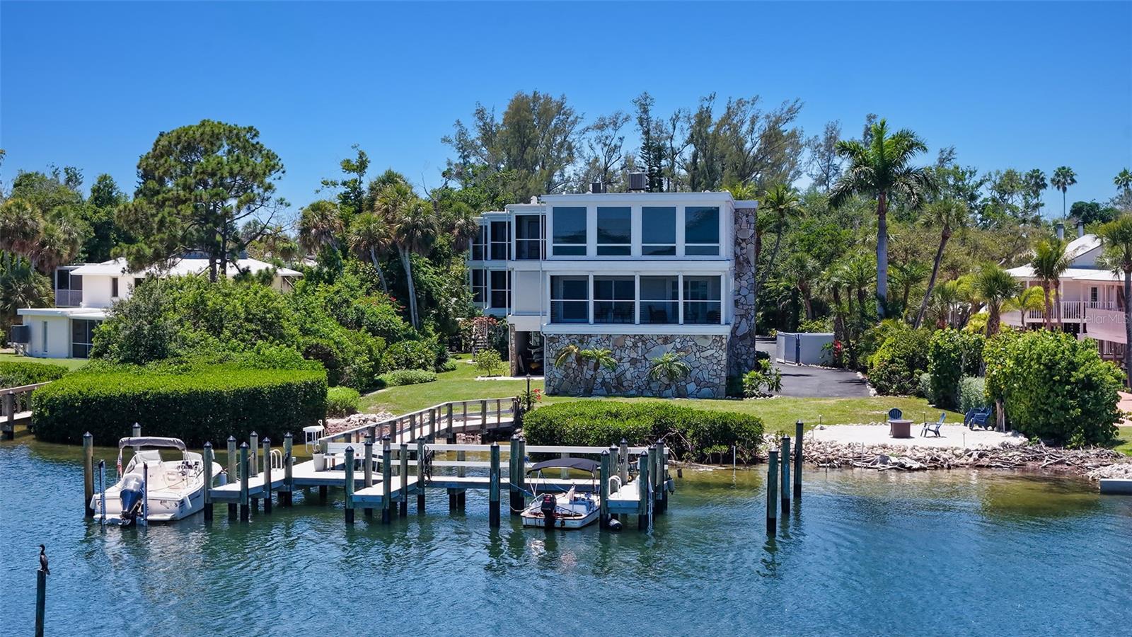 Rarely available within the intimate nine-residence bayfront community of Longboat Landing, this beautifully updated three-bedroom residence captures panoramic Sarasota Bay views and effortless waterfront living from its prized location on the north end of Longboat Key. Offered turnkey furnished and completely move-in ready, the getaway combines a refined coastal aesthetic with the rare convenience of on-site boat slips and docks (on a first-come basis) capable of accommodating up to a 26-foot vessel—creating an ideal opportunity for boating enthusiasts seeking immediate enjoyment. 
Spanning more than 1,300 square feet, the open-concept layout is filled with natural light and designed to maximize the calming bayfront setting. Contemporary wood-grain tile flooring flows throughout the residence, while crown molding, high ceilings, and chic modern finishes enhance the interiors. An extended foyer hallway leads to the sunlit great room, where walls of impact-rated floor-to-ceiling pocketing sliders open completely to the screened bayfront terrace, creating a seamless indoor-outdoor connection framed by sparkling blue water views.
The granite kitchen overlooks the main living spaces and was thoughtfully designed for both entertaining and everyday living. Features include a wraparound breakfast bar, informal dining area, solid-wood cabinetry, granite countertops and backsplash, stainless steel appliances, and generous prep space. Recent upgrades provide added peace of mind, including a 2024 A/C replacement, 2023 Hardi Plank siding installation, impact-rated windows and sliding doors throughout, kitchen and bath renovations, updated finishes, ductwork modifications, and a newer roof. 
The primary suite is positioned directly along the bayfront, offering tranquil water views and private terrace access. Two additional guest bedrooms are arranged in a split plan for privacy, including one en-suite guest suite and a third bedroom currently utilized as a home office. Completing the residence are a private laundry room, two under-building parking spaces, and additional exterior storage.
Outside, residents enjoy the relaxed waterfront lifestyle Longboat Landing is known for, with amenities including dock slips, fishing pier, heated community pool, and tennis court—all surrounded by lush tropical landscaping and Sarasota Bay vistas. 
Perfectly positioned along Gulf of Mexico Drive, this charming bayfront getaway is moments from Longboat Key’s renowned beaches, waterfront dining, boutique shopping, marinas, and scenic biking paths. St. Armands Circle and downtown Sarasota are just a short drive away, offering fine dining, galleries, theaters, Selby Gardens, and Sarasota’s vibrant cultural attractions. Rarely available, beautifully updated, and directly on Sarasota Bay, this residence offers an exceptional opportunity to embrace the best of Longboat Key waterfront living.