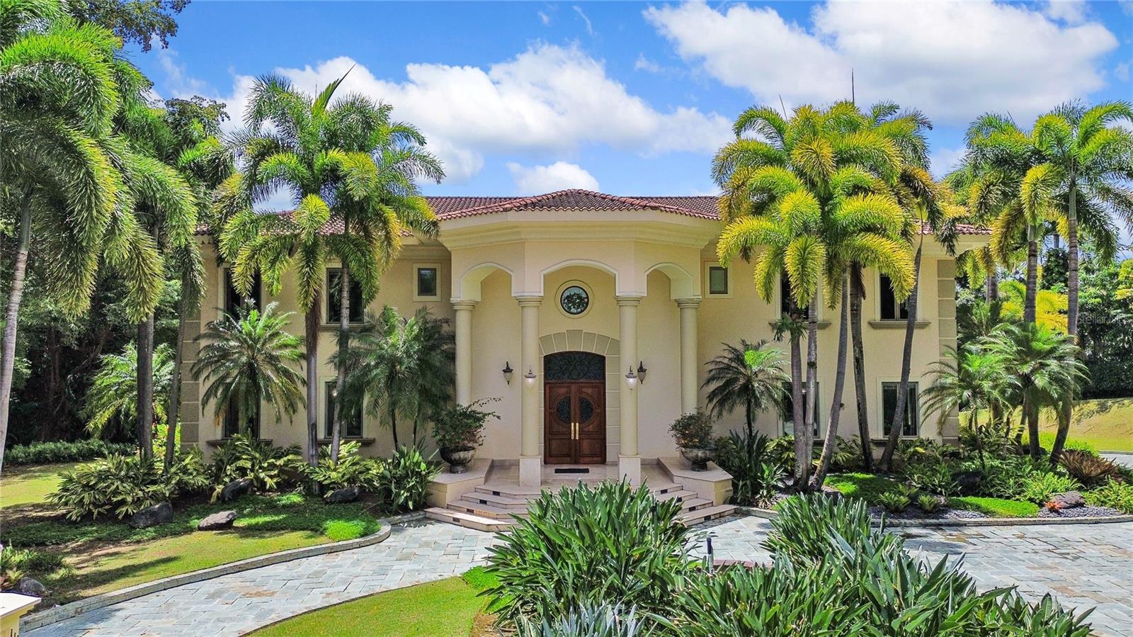 This luxurious residence is located within the exclusive enclave of San Patricio in Guaynabo. Nestled on a vast 6,248 square-meter estate and boasting 14,265 square feet of construction. A remarkable three-level estate offering elevated living, elegant design and exceptional comfort. The 5 suites, 7 bathrooms, and 1 half bath property have been meticulously designed and finished to the most exacting standards.

Thoughtfully designed residence distinguished by its scale, privacy, and seamless connection to nature. A grand driveway upon arrival, leading to an impressive main entrance. An elegant foyer with dramatic high ceilings welcomes guests with timeless sophistication. The main level is designed for family living and entertaining, boasting a fluid layout that connects the formal dining room, an exquisite living room, a private library with balcony, a cozy family room with a glass window overlooking the serene interior pool and the exterior natural surroundings. The expansive kitchen serves as the heart of the home, featuring a generous center island and a separate breakfast area. The walk-in pantry and the laundry room sit conveniently adjacent to the kitchen. For family enjoyment and relaxation, the house offers an indoor pool surrounded by vegetation and a theater room that connects to the terrace. A luxurious master bedroom with an en-suite bathroom, a sitting area and a walking closet. An exquisite terrace that opens gracefully to a dramatic staircase enhancing the home’s sense of flow and grandeur.

The second floor is conceived as a private retreat. Positioned at the heart of the bedroom wing, the family serves as a central and inviting gathering space, opening to a beautiful balcony overlooking the interior space below. This residence offers four spacious bedrooms with en-suite bathrooms, and walking closets designed for comfort and luxury living.

Thoughtfully designed to blend interior elegance with outdoor scenic surroundings. Situated on a private lot, the property is surrounded by mature landscaping, tropical foliage, and flowering gardens that create a serene and secluded setting. The outdoor areas include a stunning swimming pool, tennis court, wet bar and seating areas for comfortable alfresco living. A striking water cascade that flows from the second floor into the swimming pool.

This home also offers a three-car garage, a private gym, a playroom, his and hers bathroom, utility room for the cistern, utility room for generator, storage area, smart home control room.