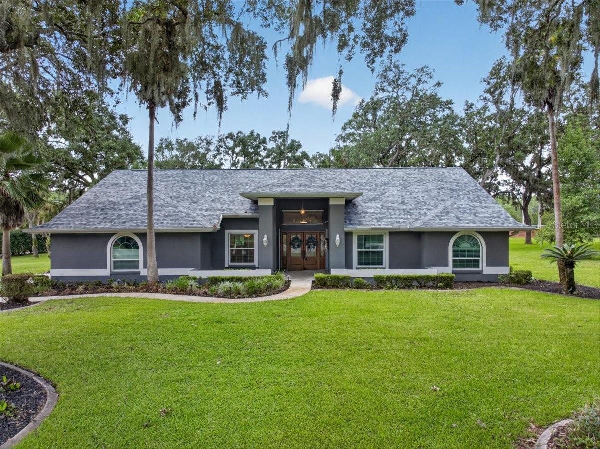 Showcased on more than an acre of park-like landscaping, with lush greenery, mature viburnum hedges and century-old live oaks, this three-bedroom plus office, three-bath pool home is located in the established gated community of Quail Ridge. Follow the long driveway beneath the oak canopy, beyond the convenient turnaround or boat-parking space to the home’s welcoming entrance. Double glass-and-wrought-iron entry doors, accented by sidelights and a transom window, open to a bright interior where travertine flooring flows through the foyer, formal dining room and kitchen. Vaulted ceilings and engineered hardwood floors enhance the living room, where a whitewashed brick wood-burning fireplace and mantel add warmth and character. The light and bright eat-in kitchen feels both polished and welcoming, with rich wood cabinetry, granite countertops, stainless steel appliances and generous workspace for everyday meals and entertaining. A pass-through connects the kitchen to the spacious Florida room, where walls of windows and impact sliding doors bring in views of the pool and expansive backyard. An adjoining office or hobby area provides generous counter space and storage cabinetry for working, creating or staying organized. Vaulted ceilings continue into the primary bedroom, where French doors open to the pool and patio. A large walk-in closet provides generous storage, while the ensuite bath features travertine flooring, a dual-sink granite vanity, jetted tub, separate walk-in shower, and built-in cabinetry for linens and additional storage. Two additional bedrooms, two full guest baths and a dedicated laundry room off the kitchen round out the home with practical comfort and everyday convenience. Step out to the screened-in saltwater pool and surrounding travertine patio, where the expansive backyard, lush greenery and mature trees create a natural backdrop for swimming, dining and relaxing. Updates and upgrades include a newer roof (2023), PGT hurricane-impact windows and two impact sliders, resurfaced pool (2023), pool enclosure rescreened (2023), new pool salt cell (2024), travertine reconditioned and sealed (2026), new well tank (2024), a whole-house water softener and filtration system, exterior paint (2024), irrigation controller rewired and solenoids replaced on all eight zones (2025), newer A/C system (2021), new bedroom carpet and fresh interior paint throughout. Located in Flood Zone X, Quail Ridge offers convenient proximity to the Veterans Expressway, providing easy access to shopping, dining, hospitals, Gulf beaches and Tampa, with Tampa International Airport approximately 30 minutes away. Classical Preparatory Charter School, serving grades K–9, is within walking distance, while the nearby 129-acre Upper Pithlachascotee River Preserve offers a playground, boardwalk and hiking trail. This home offers a spacious, country-like setting in a gated community with easy access to all that Tampa Bay has to offer.
