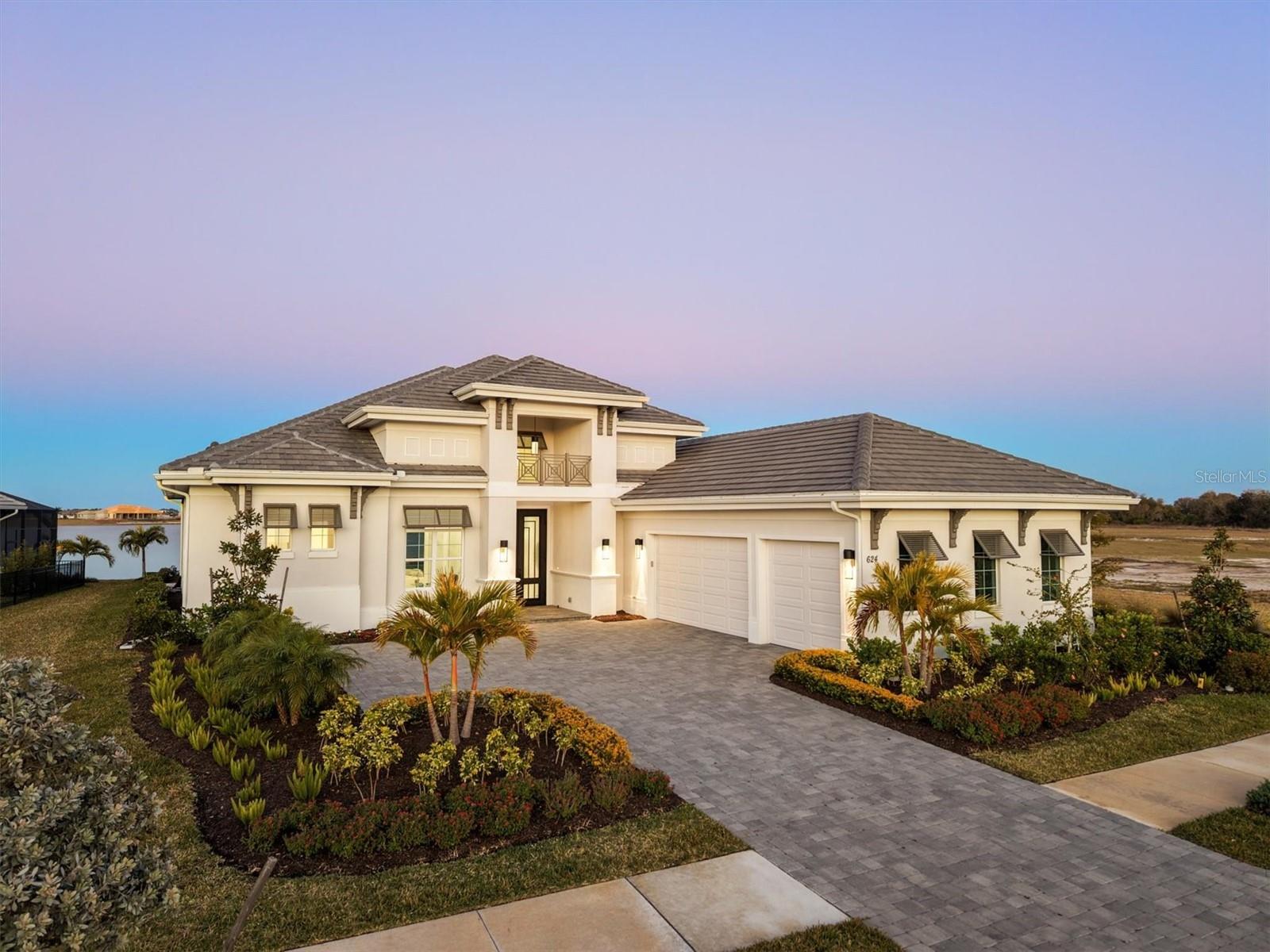 This exceptional four-bedroom, four-and-a-half-bath Madison II by Stock Luxury Homes, complete with a private office, captures breathtaking expansive lake views from nearly every room. Positioned to embrace the serene beauty of the water, this residence blends sophisticated design with effortless Florida living in one of Lakewood Ranch’s sought-after communities. A dramatic entrance begins with large custom double glass and iron doors that open into a light-filled, open-concept floor plan defined by soaring tray ceilings, stunning porcelain tile throughout and a striking wall of sliders framing uninterrupted lake vistas. Contemporary finishes and refined architectural details create an airy ambiance ideal for intimate relaxation and grand entertaining. At the heart of the home, the designer kitchen showcases premium JennAir appliances, sleek quartz countertops and custom wood cabinetry, offering beauty and function. The adjacent dining area, accented with tray ceilings and surrounded by sliders that open to the lanai along with expansive windows, allows natural light to pour in while seamlessly connecting indoor and outdoor living spaces. The private office with double French doors provides a refined workspace or quiet retreat. The spacious primary suite is a sanctuary unto itself, featuring tray ceilings, two generous walk-in closets with custom wood shelving, and sweeping views of the pool and tranquil lake beyond. The spa-inspired primary bath exudes understated luxury with a large walk-in shower, freestanding soaking tub, dual vanities and crisp contemporary finishes designed to elevate everyday living. Three additional guest bedrooms each offer en-suite baths, ensuring comfort and privacy for family and visitors alike. One guest suite is thoughtfully designed to function as bonus room if desired, with its bath also serving as the home’s pool bath for effortless outdoor entertaining. The expansive outdoor lanai is a showpiece, complete with a fully equipped outdoor kitchen and dining area, a cozy gas fireplace with seating area, and a large pool deck featuring an oversized heated pool and spa with show-stopping fire and water features. All this overlooks the sparkling lake through a panoramic screen enclosure, creating a stunning backdrop for sunset gatherings and peaceful mornings alike. In the emerging and desirable Wild Blue community at Waterside, residents enjoy resort-style amenities including tennis courts, a state-of-the-art fitness center, fishing access, and miles of scenic sidewalks for recreation and biking. Wild Blue is part of the vibrant Waterside district of Lakewood Ranch, known for its coastal-inspired architecture, curated dining and boutique shopping, vibrant community events, and proximity to Sarasota’s world-renowned beaches, arts and culture. This is lakefront luxury living redefined, refined, serene and impeccably designed for the discerning buyer.