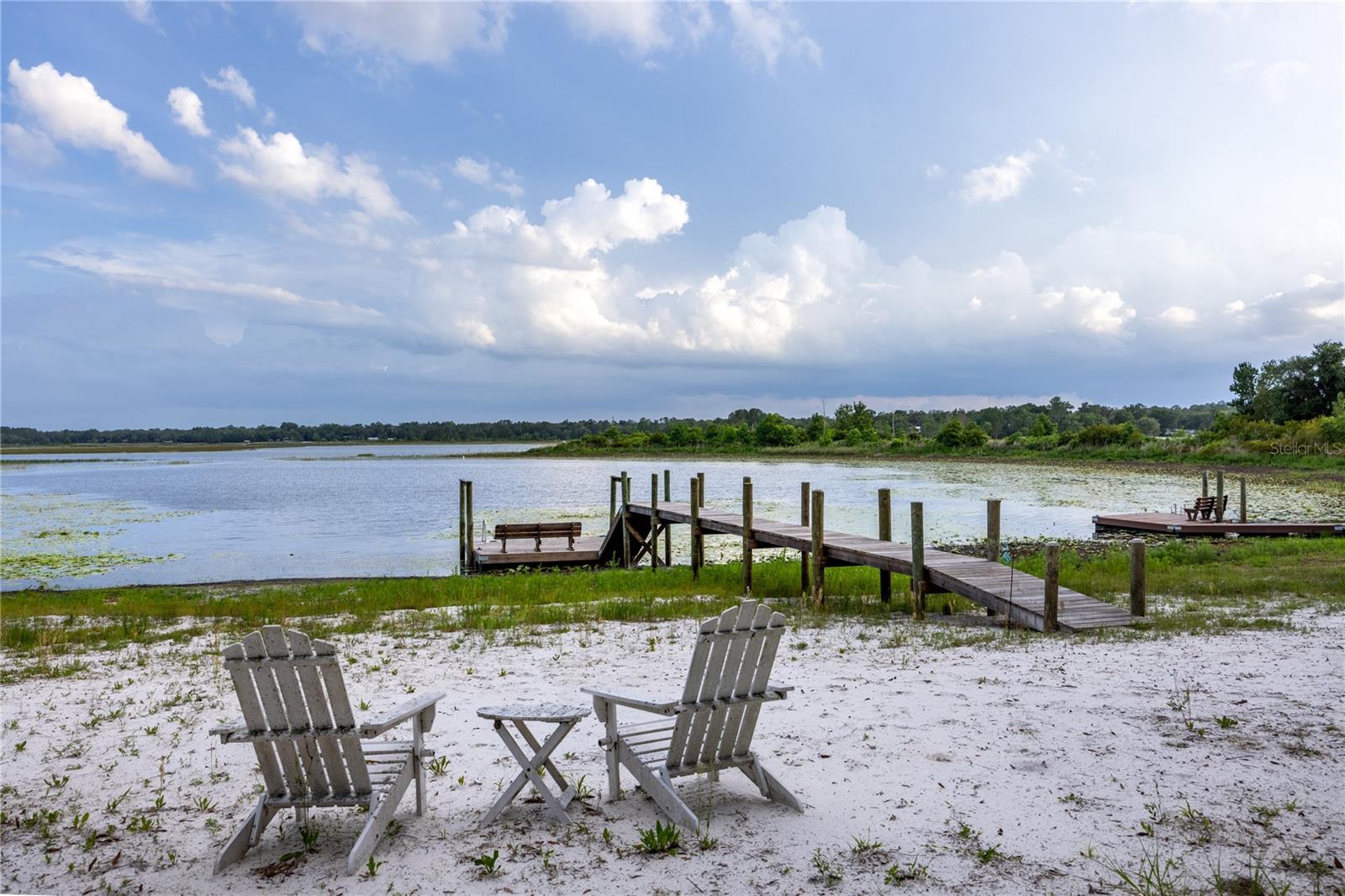 One or more photo(s) has been virtually staged. You will know this is the lakefront home you have been waiting for the moment you arrive. As you drive onto the property, you’re immediately enveloped by lush Florida greenery and towering trees that create a sense of privacy and calm and the feel of Old Florida. Along the way, the first glimpses of the lake appear, offering a preview of the beauty that defines the entire space of this lovely property that sits on almost 1.5 acres.
The property features three distinct structures, each with its own charm. The main cabin displays all cedar siding and includes three bedrooms and one bath and is 920 sq. ft, with warm antique wood paneling and floors that give it a timeless, inviting feel. The spacious kitchen easily accommodates multiple cooks, while the open great room is filled with natural light from expansive windows overlooking the lake. Whether relaxing on the couch or sharing a meal, the view is always a beautiful and serene backdrop.

Nearby, the glass house is the perfect recreational building. It is currently used for storage and offers great potential. With its all-glass walls and existing plumbing, it could easily be transformed into a unique entertainment or relaxation space. Just beside it sits the Cottage, a cozy 420 sq. ft., two-room retreat complete with its own bathroom. It features a sitting area with large windows facing the lake, as well as a generous space for a bed and dresser—perfect for guests or quiet escapes. You will enjoy a brand new deck area that has just been constructed on the Cottage that provides the perfect area for overlooking the lake with your morning coffee. 

Stepping into the backyard feels like stepping back in time, surrounded by majestic Florida oak trees draped in Spanish moss. The true centerpiece of the property, however, is the lake itself. Lake Cowpen is approximately 650 acres and is perfect for fishing and recreation. A sandy beach area invites you to unwind, while a large newer dock is perfect for fishing or launching kayaks. There’s a lakeside fire pit for cozy evenings, and at night, the stars stretch endlessly across the sky, creating moments of quiet awe. A covered carport with an attached storage room adds both convenience and functionality and would make the perfect area for a shop. Beneath a sprawling oak tree sits a table and chairs that creates opportunity for talking, laughing, and enjoying the gentle lake breeze. It’s a place of connection and stillness.

There have been many upgrades and improvements made in the last few years that the new owners will enjoy, including:  
brand new paint on the exterior of the cottage and the enclosed recreational building, newly constructed porch and railing of the cottage, new woodwork on the back of main cabin, Foundation re-stabilization ($10,000), beach sand, new floating dock and walkway ($15,900), new lighting and fans along with new exterior lighting. 

With its three unique structures and abundant space, this property offers both versatility and tranquility. Above all, the lake house is a peaceful and rustic retreat—one that feels both timeless and deeply personal. 
You are invited to come see if this peaceful way of life suits you - you may never want to leave!