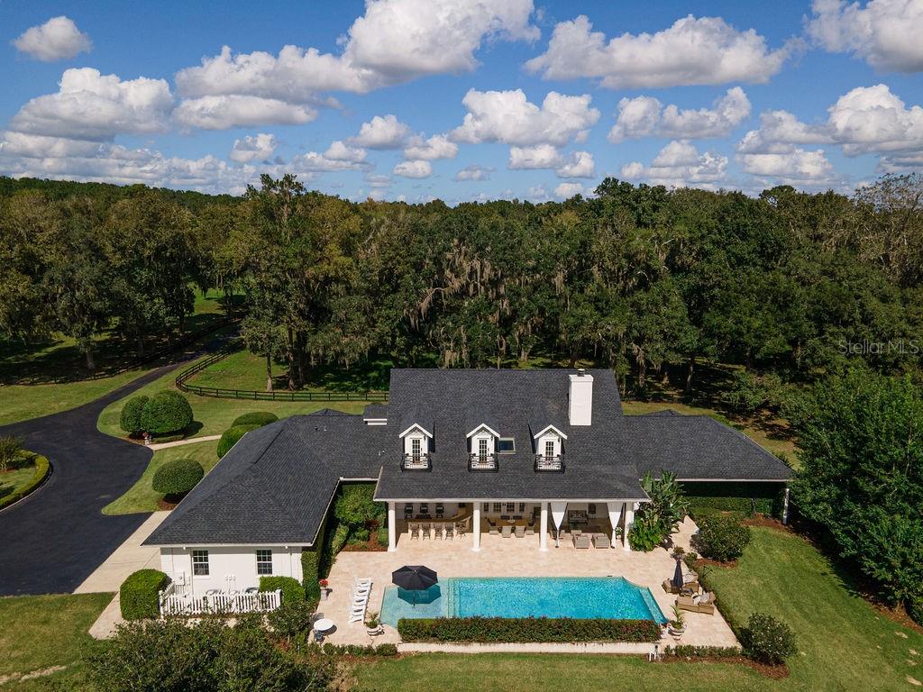 Escape to your own private oasis with this luxurious gated estate, a rare find located on a picturesque 10-acre property on the highly desirable southeast side. This location offers the perfect blend of privacy and convenience. Step inside the main house, an elegant four-bedroom home that exudes comfort. The primary suite is a true sanctuary, featuring an expansive walk-in closet with an island, dual baths, and a spa-like room with a soaking tub, an elegant chandelier, and a walk-out patio surrounded by birds of paradise. The heart of the home is the open-concept custom dream kitchen, with meticulous wood details, including crown moldings and a generously sized Calcutta marble island. The private dining room, with its stunning Restoration Hardware table, shiplap walls, and soaring 15-foot ceilings, provides the ideal space for intimate gatherings. Indulge in resort-style living as you step outside into your own personal retreat. Open the French doors from the living room and be greeted by a grand heated saltwater pool, much like a luxury hotel. Entertain with ease at the outdoor bar and kitchen or cozy up by the fireplace for relaxation. This exceptional property also includes a large matching two-bedroom guest house, perfect for accommodating visitors or extended family members. If you’re considering pleasure horses at the property, there is a shaded paddock area specifically designed for them with space for a barn. Embrace the equestrian lifestyle without the hassle of maintaining a large farm. With a newer roof and proximity to downtown, hospitals, and gourmet restaurants, this estate offers comfort, convenience, and privacy. Around the corner is the Bellechase Gated Community and sought-after private schools. It's also a short drive to Florida Horse Park, HITS, and the World Equestrian Center.