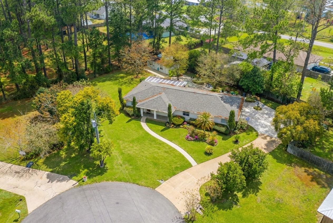 Located at the end of a CUL-DE-SAC on a private ½-ACRE LOT, this cared-for 3-bed, 2-bath home offers privacy, flexible living space, and exceptional utility features. Mature landscaping surrounds the home, creating a peaceful setting with NO VISIBLE NEIGHBORS. Inside, you’ll find spacious rooms, TILE FLOORING THROUGHOUT, and crown molding with integrated lighting. The primary suite includes a GENEROUS WALK-IN CLOSET, double vanity, and soaker tub with separate shower. The SPLIT FLOOR PLAN is designed to allow for a POTENTIAL IN-LAW SUITE, including one bedroom with sink, cabinetry, and exterior access across the hall from a second generously sized guest bedroom, and a full bathroom. A large indoor UTILITY AND LAUNDRY ROOM provides additional storage, complemented by a separate storage room in the two car garage. Outdoor living and functionality are standout features, with a LARGE PAVED PATIO, SCREENED SUNROOM, and two outbuildings. One shed includes a climate-controlled WORKSHOP and STORAGE ROOM, the second is a large METAL BUILDING with shelving. The home features a GAS STOVE, GAS DRYER, GAS ON-DEMAND WATER HEATER, AND A GAS FIREPLACE—features rarely found in Florida homes—along with a generator plug, irrigation system, and well water treatment system. Major updates include a NEW ROOF. Conveniently located only 2 miles from Publix, Walmart, and a hospital, this home offers privacy, versatility, and space rarely found so close to town.