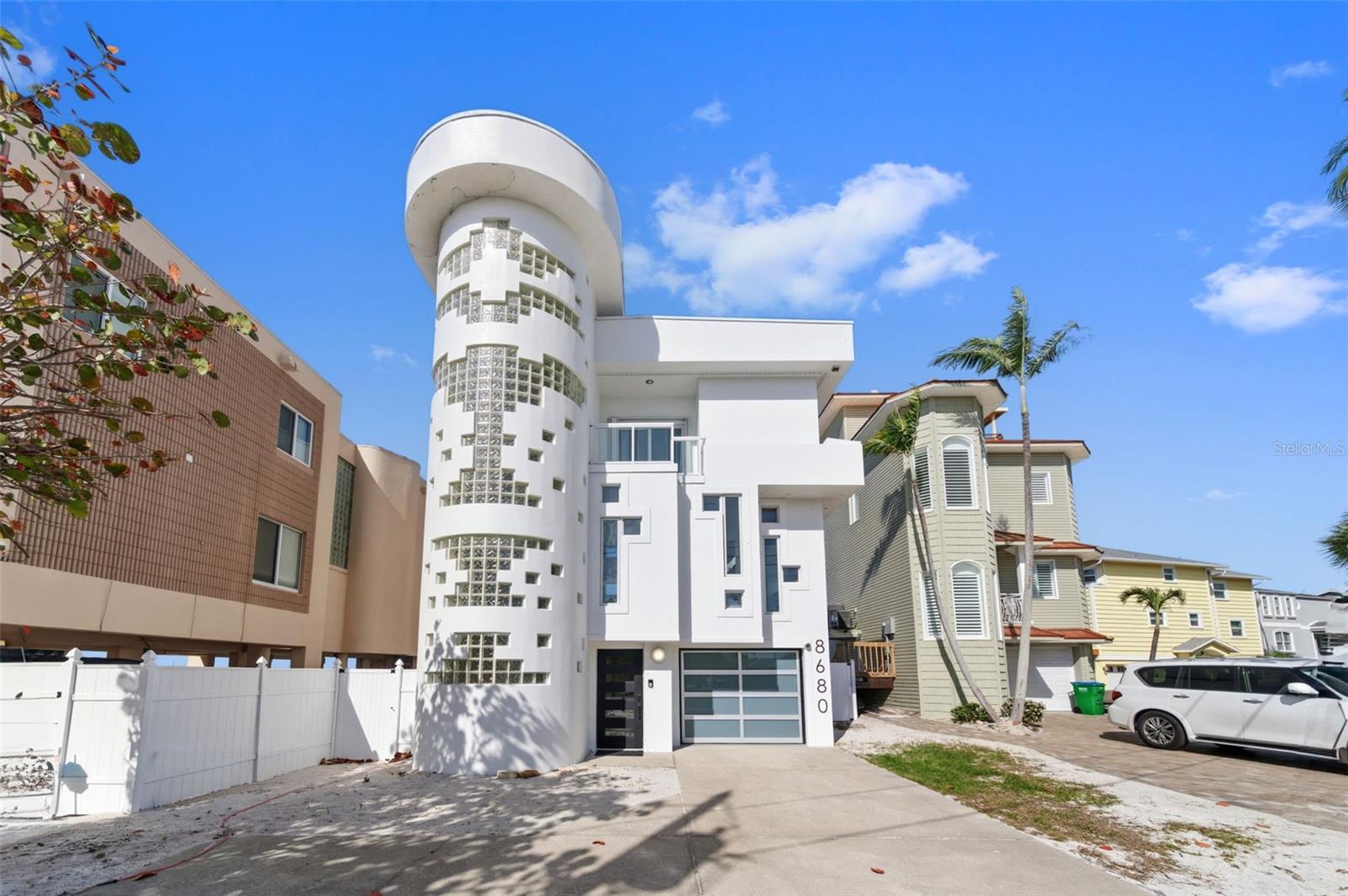 Sunset Beach’s iconic “Glass Block Home,” masterfully envisioned by acclaimed architect Daniel Thayer Dawson, is now available—presenting a rare opportunity to own one of Florida’s West Coast’s most architecturally distinctive residences. Perfectly positioned along the pristine shores of the Gulf of Mexico, this striking three-story contemporary beachfront retreat showcases dramatic 20-foot floor-to-ceiling windows, blending sleek modern design with effortless coastal sophistication.
Inside, the home offers a seamless balance of form and function. The soaring glass walls in the living room flood the interior with natural light while framing breathtaking panoramic views of turquoise waters and unforgettable Gulf sunsets. An open-concept layout enhances the sense of space and flow, creating an inviting atmosphere ideal for both everyday living and elegant entertaining.
The chef’s kitchen is thoughtfully designed with a state-of-the-art induction cooktop, custom cabinetry, and counter seating for four—perfect for casual dining or gathering with guests. The adjacent living area, defined by its 20-foot ceilings and refined designer finishes, provides a stunning yet comfortable setting for hosting or relaxing.
The primary suite serves as a tranquil sanctuary, offering sweeping water views and direct access to a private porch—an ideal place to unwind while watching the sunset or moonlight dance across the Gulf. The spa-inspired ensuite bath features a walk-in shower and a calming, modern aesthetic.
A dramatic floating glass walkway leads to the third floor, where a guest bedroom enjoys its own spectacular beach views. An additional bedroom is also located on this level. Each guest suite is designed for comfort and privacy, complete with its own ensuite bath and private porch overlooking the water.
Outdoors, the home transforms into a private beachfront oasis. Multiple expansive decks with custom glass railings provide uninterrupted views, creating the perfect setting for sunbathing, entertaining, or dining under the stars. With direct beach access, every day feels like a getaway.
Enhancing both convenience and luxury, a striking glass elevator connects all three levels of the home. The ground floor features a freshly updated two-car garage with a new commercial-grade epoxy finish, and ample storage room as well.  A rear garage exit opens to a covered lanai with direct beach access, along with a spiral staircase leading to the main living areas.
Just a short one-minute walk along the sand brings you to the famous beachfront destination of Caddy’s and the lively and equally famous Ka’Tiki Bar & Gril.  Both offer daily live music in a vibrant coastal setting. Whether you’re seeking peaceful beachfront relaxation or a more social atmosphere, this exceptional location offers the best of both worlds.
Experience the unmatched design and coastal lifestyle of Sunset Beach’s Glass Block Home—schedule your private showing today.
