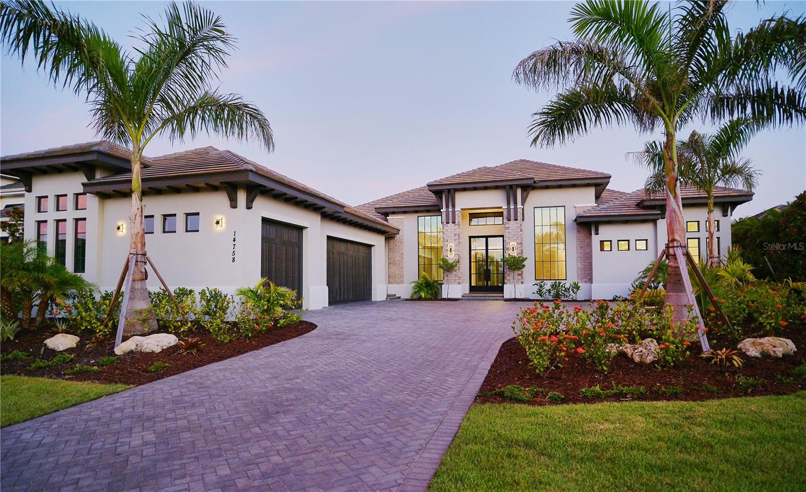 NEW CONSTRUCTION!!! Transitional West Indies Custom Home by John Cannon Homes.
Experience the perfect blend of West Indies architecture with contemporary influences in this brand-new, never occupied custom residence. From the moment you arrive, huge tandem windows, a striking 10-foot custom iron entry door and a symmetrical façade draw your eyes straight through to the breathtaking rear views. Inside, the cathedral ceilings with scissor beams in the great room flow seamlessly to the main lanai and through the expansive pool enclosure. 10-foot accordion stacking doors topped with transom windows open the home to true indoor–outdoor living. A gas fireplace with cultured stone surround and mantle creates a warm focal point, while a climate-controlled wine room with illuminated agate stone panels adds an element of artistry. The home offers both a primary kitchen and a chef’s prep kitchen, each outfitted with high-end appliances. Natural light floods the space through an interior/exterior window and skylights. Two secondary bedrooms each feature en suite baths and walk-in closets. A versatile bonus room includes a disappearing corner door to extend entertaining space to the outdoors. In the owner's wing, you’ll find dual owner’s baths and closets—each closet with LED pin lighting and custom built-in cabinetry. A private owner's courtyard with outdoor shower and composite decking creates a resort-like retreat.
The rear lanai is fully equipped with an outdoor kitchen and island, overlooking the stunning pool area enclosed by a clear-view screen and colonnade. The pool features shellock pavers, a large sun shelf with cascade bubbler, in-pool lounge chairs, and a floating fire pit with mirrored granite edges. The negative-edge spa with glass waterline tile completes the scene. This smart home comes pre-wired for electric window treatments, and includes an integrated camera system, home music, and more—delivering luxury, comfort, and technology in one extraordinary package.