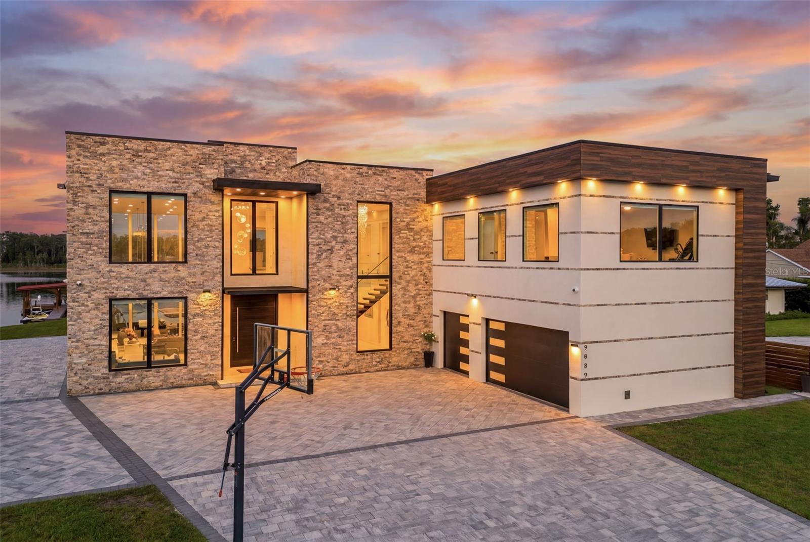 Wake up to a beautiful fire-lit sunrise over the water. On a private 1.6-acre lot with 150 feet of frontage along 83-acre Lake Georgia, a rare ski-friendly lake in East Orlando, 9889 Lake Georgia Drive is an extraordinary custom-built lakefront estate where every detail has been sourced, engineered and installed at the highest level. Offering five bedrooms and six and one-half baths, this is a home defined by scale and craftsmanship. Pass through the sliding gated entry, follow the brick-paved driveway toward the striking custom pivot door, framed in limestone and accented with Turkish stone, and you understand immediately that this is no ordinary address. Inside, the home opens dramatically as 48-by-48-inch porcelain tile floors extend beneath soaring volume ceilings, flanked by floor-to-ceiling windows that draw the lake directly into the living space. Custom floating stairs rise with sculptural elegance beside a crystal chandelier and glass railings, while curated designer lighting sets a tone of refined permanence throughout. A stacked-stone fireplace anchors the great room, and a wet bar with gas fireplace extends the entertaining space. The chef's kitchen is anchored by a large waterfall-edge quartz island, complemented by German custom high-gloss cabinetry, premium stainless steel appliances, a built-in Thermador espresso machine and a porcelain tile backsplash. A walk-in pantry adds everyday function to a home designed to be lived in as beautifully as it looks. The primary suite offers lake views, dual quartz vanities, glass-enclosed rain showers, a handheld bidet and a walk-in closet with custom organizers. Additional en-suite bedrooms feature luxury vinyl plank floors and designer baths with backlit mirrors and matte fixtures. Most rooms are wired for interior and exterior audio, with surround sound in the media and family rooms, all controllable by phone or remote. A dedicated home office, a game/media room ready for billiards, and a second-floor loft complete the interior. Outside, resort-caliber amenities await. A magnificent summer kitchen is outfitted with a 48-inch barbecue, four gas burners, granite counters, ice maker, mini-refrigerator and sink, all beneath a tongue-and-groove wood porch ceiling with automatic screens. The newly resurfaced lap pool features a spa, sun deck, water feature and Pebble Tec surface, surrounded by 2,000 square feet of paver decking and adjoined by a nine-person spa. Above, a balcony finished with artificial turf delivers panoramic lake views. On the water, a large covered boat dock with upper deck, boat hoist, private slip and Sea-Doo storage, plus a private boat ramp on site, completes the picture. Additional highlights include a 22,000-kilowatt generator, dual tankless water heaters, water filtration and softening, $25,000 in motorized custom blinds throughout, an insulated three-car garage with refinished floors and custom storage racks, a security surveillance system, LED lighting, gas-infused double-pane windows and doors, a lake-fed irrigation system and parking for 12-plus vehicles. Ideally located, zoned for Winter Park schools with an Orlando address, just over three miles from UCF and the Central Florida Research Park, home to Lockheed Martin, Northrop Grumman, Raytheon, Boeing and L3Harris. Downtown Orlando and Orlando Health and AdventHealth medical centers are roughly 12 miles west, while Park Avenue's boutiques and dining are minutes away. This is lakefront living at its best.