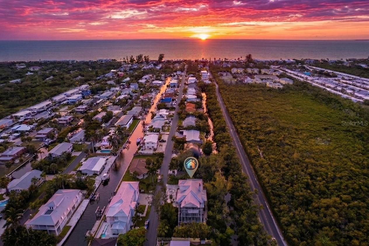 Longboat Key Waterfront Home combining Canal frontage & Deeded Beach Access. Key West-style home featuring 4-beds, 3.5-baths offering 2,688 SF on a .32-acre lot with 154 feet of canal waterfrontage. Elevated, engineered for storms, and built in 2007built in 2007 with concrete block construction, Hardie board siding, hurricane impact windows and doors, and a standing seam metal roof. A classic Key West-inspired design with an expansive wraparound porch, Barbados-style railings, and mature tropical landscaping creates an immediate sense of arrival. The paved driveway leads to a 2-car garage with an air-conditioned storage closet. Step through the beveled glass entry door with sidelights and into a grand living room with soaring 22-foot ceilings, a wood-burning fireplace, and a sweeping staircase that anchors the space. Plantation shutters throughout the home enhance the island vibe. The main living level is open and connected. The kitchen is outfitted with a center island, dual sinks, stainless steel appliances, stone countertops, dual pantries, and separate dining areas. A comfortable den is ideal for reading or watching the game, while a main-level office and bedroom with a full bath serve perfectly as a guest suite or in-law accommodation. Upstairs, the owner's suite is a genuine island escape. Two walk-in closets, two sets of glass French doors opening to an expansive private covered balcony. Spa-inspired bathroom with limestone floors, dual sinks, a soaking tub, and a separate shower. Two additional guest bedrooms share a full bathroom and a dedicated laundry area, each with its own balcony offering peaceful views. Throughout the home, wide-plank hardwood and travertine tile flooring, 8-foot doors, window seating, French doors, custom lighting, and custom bathroom tile showcase craftsmanship and quality. Outside, a large heated pool and spa sit within a beautifully landscaped two-story screened enclosure, with a pavered walkway leading to the dock at the water's edge — ready for your boat, kayak, or simply an evening watching the dolphins and manatees pass by. A screened lanai overlooks the canal, the perfect spot for a morning coffee or an evening cocktail. You are just four homes from Sarasota Bay with direct boating access in minutes and no bridges to open water. Deeded beach access to the Gulf of Mexico is directly across the street, where nightly sunsets are a daily ritual and the powdery sand of the Gulf shoreline is your backyard extension. Joan Durante Park is a short distance away. The neighborhood allows monthly rentals with an optional HOA — seasonal rental potential OK. The dining and lifestyle amenities: Harry's Continental Kitchen, Euphemia Haye and Loft, Shore Restaurant, and Drydock Waterfront Grill w/waterfront dining. The Longboat Key Club's two championship golf courses mean you never have to leave the island. The St. Regis Longboat Key, famous St. Armands Circle, and the energy of Sarasota. Sold furnished.