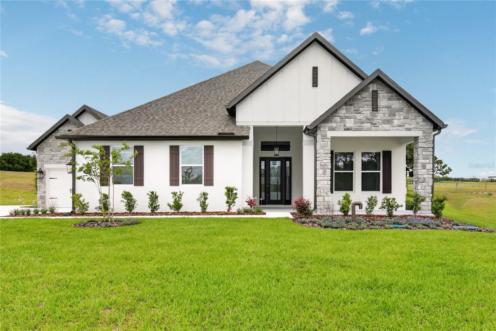 Welcome to Waycross, a spacious and thoughtfully designed four-bedroom, three-bath home with a three-car garage, located in the new Saddle Hill community in Fruitland Park. From the inviting covered front porch to the wide, welcoming foyer, this home offers a seamless blend of comfort and functionality. The open-concept layout features expansive main living areas, where the family room, kitchen, and breakfast area flow together effortlessly—ideal for everyday living and entertaining. The kitchen showcases a large breakfast bar, walk-in pantry, quartz countertops, bright white cabinetry, stainless steel appliances, modern tile backsplash, and matte black hardware. A separate dining area provides additional space for formal or casual gatherings. French doors open to a covered outdoor kitchen, extending the living space and creating an ideal setting for outdoor relaxation or entertaining. A dedicated media room offers flexible space for a home theater, game room, or additional living area. The primary suite is located at the rear of the home for added privacy and features a spacious bedroom, spa-inspired bathroom with soaking tub, walk-in shower, and a large walk-in closet. Secondary bedrooms are well-positioned to provide comfort and flexibility for family or guests. Saddle Hill offers a peaceful, tree-lined setting while remaining conveniently close to shopping, dining, recreation, and everyday amenities. Enjoy nearby Lake Griffin, local golf courses, and the charm of surrounding communities.