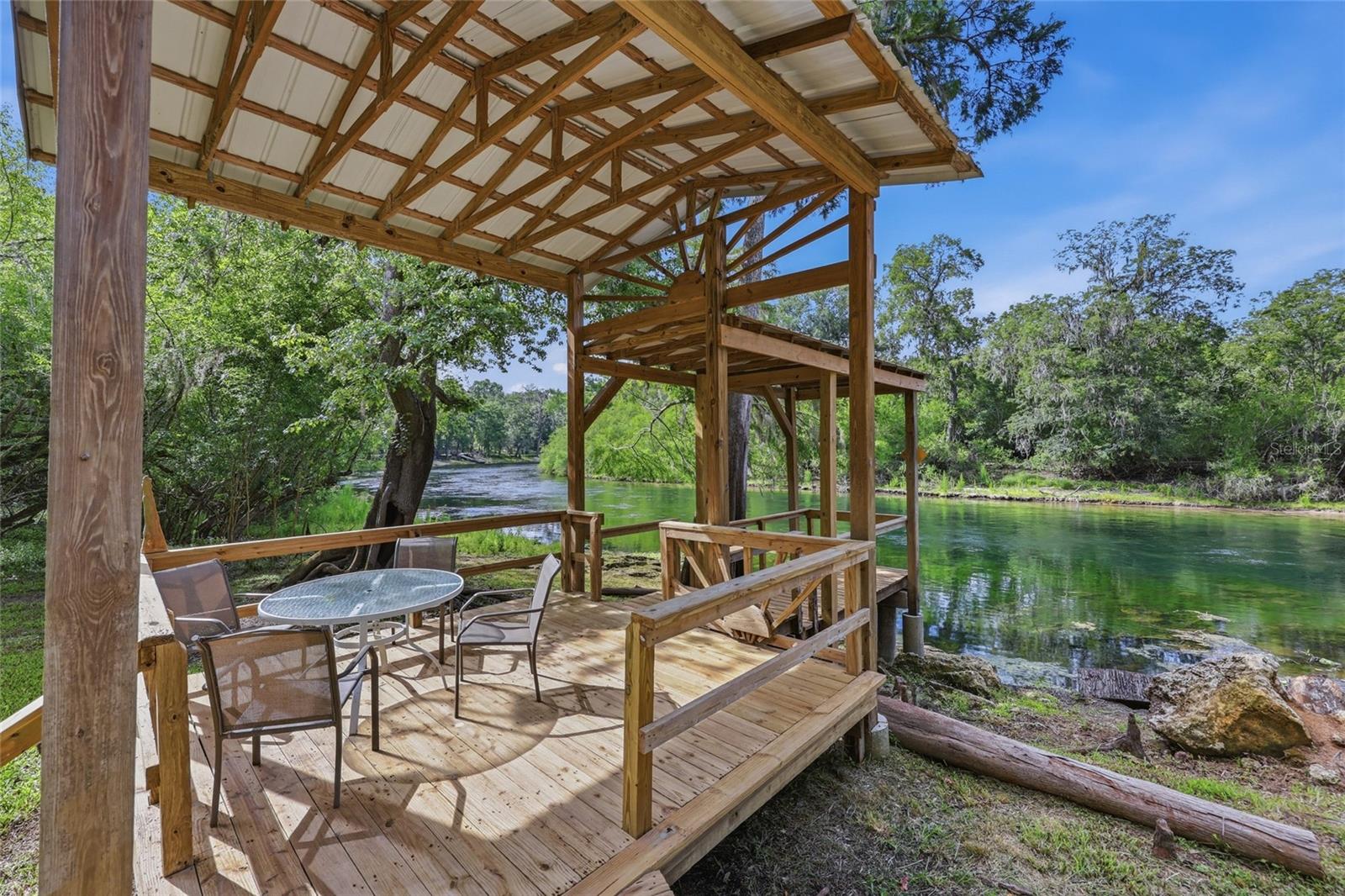 Remarkable rare opportunity to own approx 2 acres on the Santa Fe River in the highly sought-after Three Rivers Estates community on a double lot. This cabin-style river home is perfectly positioned on a scenic bend in the river, offering views both upstream and downstream. Designed to enjoy the waterfront setting, the home features wraparound porches, a massive rear deck overlooking the river, and a private boardwalk that winds through impressive cypress trees to a covered riverside deck. Inside are 2 bedrooms, 1 full bathroom, a sunroom with river views, and a wood-burning stove. The lower level offers a partially finished game room with a half bath and additional storage space. Outside, you'll also find a full walk-in outdoor shower and a garage/storage area perfect for a golf cart, lawn mower, or all of your river toys. A new roof was installed in 2025. Three Rivers Estates property owners enjoy exclusive access to multiple private parks with boat ramps on both the Santa Fe and Ichetucknee Rivers, providing endless opportunities for boating, kayaking, tubing, paddleboarding, and fishing. The property is just minutes from Ichetucknee Springs, Ginnie Springs, Poe Springs, Blue Springs, Rum Island, and several other North Florida springs. Whether you're looking for a private river retreat, a full-time residence, or an income-producing short-term rental, this is a rare opportunity to own one of the Santa Fe River's most desirable waterfront locations.
