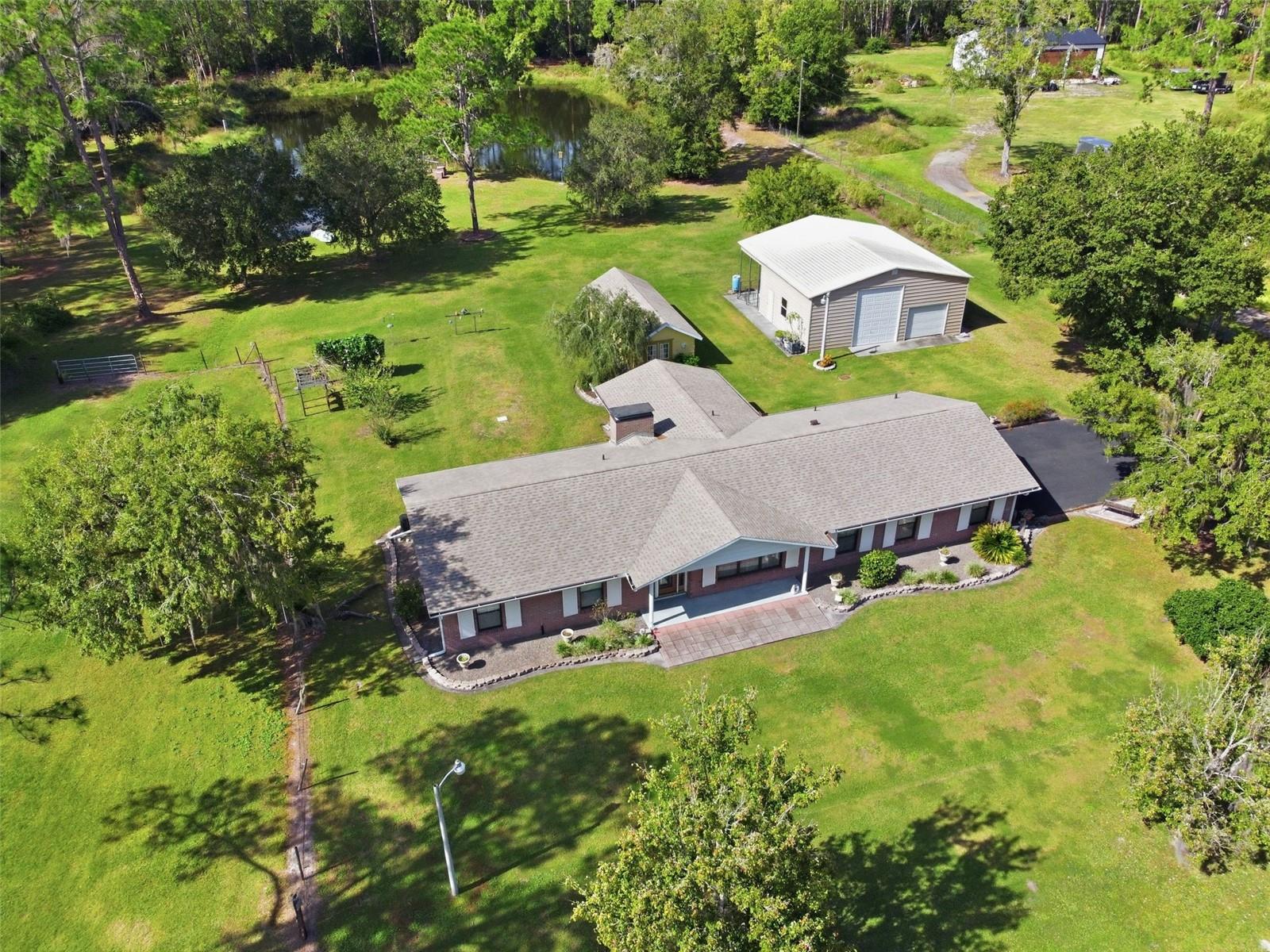 Discover the beauty of peaceful rural living at 9240 Moore Road in Lakeland, Florida. A rare 4-acre private estate where wide-open spaces, mature oak trees, and modern comforts come together to create the perfect country retreat. With NO HOA, Flood Zone X, and plenty of room to spread out, this beautifully remodeled 3-bedroom, 2-bathroom block home offers the privacy and serenity that's becoming harder to find. Wake up to wildlife, spend your afternoons fishing from your private pond with extended dock, or relax in the climate-controlled Florida room overlooking the water. Inside, you'll find updates galore, including engineered hardwood and tile flooring, energy-efficient windows, a cozy wood-burning fireplace, and a beautifully updated kitchen featuring solid wood cabinetry, pull-out shelving, a GE Café range, and LG stainless steel appliances. Major updates—including a 2022 roof, Trane 19 SEER HVAC with heat pump, tankless water heater, water softener, updated fixtures, and hurricane-rated plantation shutters—provide exceptional peace of mind. Outside, the impressive 36' x 36' steel workshop is ideal for RVs, boats, hobbies, or a home business, while a fenced pasture for horses or livestock, a block garden shed, private shooting range, electric gated entry, asphalt driveway, and security system with cameras complete this one-of-a-kind property. If you've been dreaming of a private country home with acreage in Lakeland where you can enjoy the quiet of nature without sacrificing convenience, this extraordinary estate offers the lifestyle you've been waiting for.