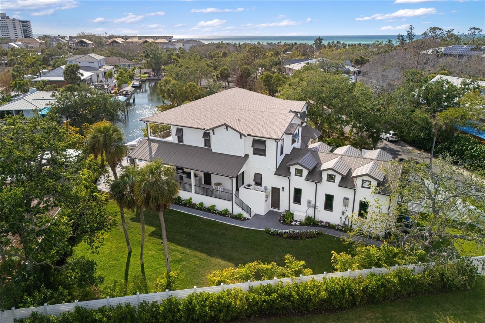 Start living your dream lifestyle on world-famous Siesta Key in this Pham Development custom-built waterfront British West Indies–style home. Located on a quiet street on the north end of the key—close to the beach, Siesta Key Village and Out-of-Door Academy—and just minutes on and off the island, this residence offers island living at its best. Set on a corner canal-front lot, the two-story home features 5 bedrooms, 5 full bathrooms and 1 half bath, with 3,875 square feet under air, a great room floor plan, soaring 22-foot vaulted ceilings, and walls of windows and doors—including large pocket sliders—that bring in abundant natural light and seamlessly connect indoor and outdoor living.

The adjacent dining area provides ample space for entertaining, while the stunning kitchen—completely open to the great room—serves as the heart of the home with a large 9-foot island with extended seating, professional stainless steel gas appliances and a walk-in butler’s pantry. The home also features a fully integrated security system, whole-home sound system and a complete Control4 smart home system. The first-floor owner’s suite offers a private retreat with a walk-in shower, freestanding tub, dual vanities, and a large custom walk-in closet. A laundry room, powder room and mudroom complete the first level, and a 3-car garage provides ample parking and storage.

Upstairs you’ll find four en-suite guest bedrooms, an additional laundry area to service them, and an expansive second-level balcony to take in the views. Outdoor living includes approximately 1,502 square feet of covered lanai, an exterior wrap-around porch, and balcony space designed for enjoying the island lifestyle, complete with SunBrite outdoor TVs, and Brazilian hardwood ceilings. The privately gated driveway and fully fenced property are surrounded by lush landscaping, creating a secluded tropical setting with a large swimming pool, champagne spa and expansive pool deck perfect for relaxing or entertaining. A private well supports irrigation. With 31 linear feet of canal frontage, the property features a 31-by-12-foot electric boat lift rated for 6,500 pounds, two jet ski ramps and about a 4.5-foot draft—ideal for boating and enjoying the water, making this oasis the perfect place to enjoy the Siesta Key lifestyle.