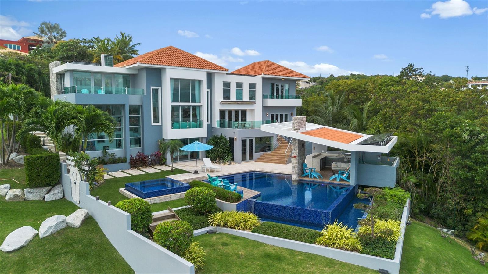 Welcome to 12 and 13 Roble Valley, a private estate within the sought-after Palmas del Mar community in Puerto Rico. This is the only luxury property in Palmas offering complete and permanent privacy, paired with commanding panoramic views of the Caribbean Sea, the surrounding islands, Puerto Rico’s eastern coastline, and the breathtaking El Yunque Rainforest mountain range.

The 5 bedroom, 6 bathroom main residence at 13 Roble Valley is the crown jewel of Palmas del Mar. Paired with the most coveted and breathtaking adjacent lot at 12 Roble Valley, this offering creates a rare opportunity to secure your own private sanctuary, preserved exactly as you wish for years to come.

The home on 13 Roble Valley was completed in 2016 and meticulously maintained by its original and only owners and sits in a category entirely its own. With no neighboring properties to the left or right, every window, terrace, and balcony opens to uninterrupted natural beauty. What you experience here is silence, space, and a sense of seclusion that simply does not exist elsewhere in Palmas del Mar.

The main residence offers five bedrooms, six bathrooms, and approximately 5,000 square feet of refined indoor living. Soaring 13 foot ceilings and expansive custom windows flood the home with natural light and elevate every room with scale and drama.

Only the finest finishes were selected throughout, and each bathroom has been designed as a statement, blending luxury with artistry.

The outdoor living experience is nothing short of extraordinary. The backyard is a private resort, featuring a stunning pool and jacuzzi, a covered BBQ area ideal for entertaining, and a fully equipped indoor gym, all set against a backdrop of lush greenery, ocean views, and open sky, and complemented by a one of a kind outdoor bathroom and shower that allows you to rinse off or unwind while taking in panoramic views of the Caribbean Sea and surrounding islands.

The adjacent lot at 12 Roble Valley has been transformed into a remarkable Greek inspired amphitheater, crafted with 276 one ton boulders to create a serene and magical scene.

With a pergola, fire pit, and storage shed already in place, this space is perfect for gatherings, quiet reflection, or unforgettable evenings under the stars, all while preserving the estate’s unmatched privacy.

This home is as resilient as it is beautiful. Forty one solar panels, three Tesla Powerwalls, a whole house generator, and a 400 gallon rainwater cistern ensure energy independence, security, and peace of mind year round.   

Offered fully furnished and truly turnkey, this estate allows you to step immediately into a lifestyle defined by privacy, elegance, and natural splendor. If you are seeking the rarest offering in the Caribbean, a property that cannot be replicated, 12 and 13 Roble Valley is that opportunity.