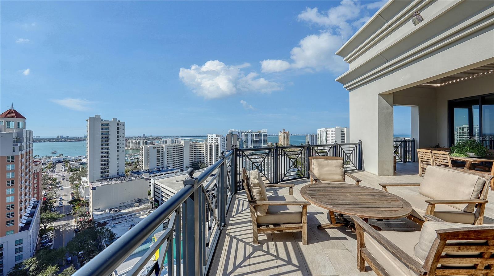 Perched atop The Plaza at Five Points in the heart of downtown Sarasota, this exceptional penthouse offers an unrivaled blend of sophistication, breathtaking bay and city views, and unparalleled craftsmanship. Designed by Westwater Construction, this residence redefines luxury with meticulous attention to detail and an expansive layout that feels like a private estate. Every room is designed to maximize panoramic vistas, with floor-to-ceiling windows and two expansive terraces that invite seamless indoor-outdoor living. A dual-sided gas fireplace, framed by custom shell stone, serves as a focal point in the open living room, enhanced by dimmable lighting to create the perfect ambiance. A dedicated formal dining area with extensive bar, an office with custom built-ins, and family room offer both functionality and elegance. The chef’s kitchen is a masterpiece of design. Custom Australian walnut cabinetry and Cristallo quartzite countertops are complemented by an array of professional-grade appliances, including a Wolf six-burner dual-fuel range with griddle, convection ovens, and a built-in steam oven. A handcrafted CopperSmith range hood, dual Rachiele copper sinks with Waterstone faucets, an instant hot water dispenser, and a built-in Wolf coffee station further elevate this space. A Sub-Zero Designer Series refrigerator/freezer and island ensure ample storage, while a built-in desk provides convenience. The Fine Art handcrafted Foret chandelier adds the prefect touch of artistry. Wine connoisseurs will appreciate the custom bar area, crowned with a striking Sahara Noir marble countertop and illuminated by sommelier chandeliers made from repurposed wine bottles. A temperature-controlled wine room holds 300 bottles and completes this indulgent area. The primary suite is a serene retreat with private terrace access and an elegant en-suite bath featuring spa-inspired finishes. Two additional bedroom suites with walk-in closets also enjoy terrace access. The expansive outdoor spaces extend the living area, offering the ultimate setting for relaxation and entertainment. A custom-built Ipe bench surrounds a sleek fire table, while a fully equipped summer kitchen with a Lynx grill, sink, and electronic louvered roof allows for effortless alfresco dining. Lush built-in planters enhance the urban oasis, creating a serene escape above the city. Additional conveniences include two secure under-building parking spaces and a private storage unit. Residents of The Plaza enjoy access to a full suite of five-star amenities, including concierge services, valet parking, grilling area, rooftop pool deck with cabana, and a state-of-the-art fitness center. Located just steps from Sarasota’s finest dining, shopping, and cultural attractions, this penthouse presents a rare opportunity to experience downtown living at its most refined.