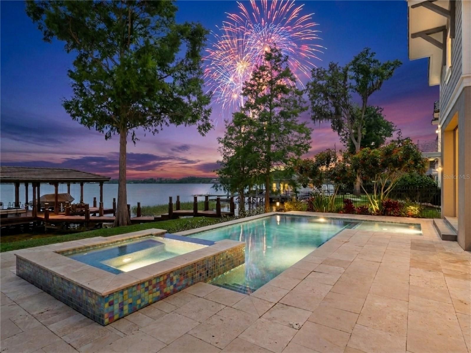 Under contract-accepting backup offers. One or more photo(s) has been virtually staged. A Custom Estate on one of the Butler Chain's most coveted stretches of shoreline. Situated near the tip of a peninsula lot, the home captures panoramic water views of Lake Tibet, Lake Sheen, and the connecting canal from nearly every room. The south-facing rear orientation delivers sunrises over the water each morning, golden sunsets each evening, and nightly Disney World and EPCOT fireworks reflected across the lake after dark. The Disney Springs hot air balloon is visible from the yard. Step from the back of the home directly to your private dock and boat lift on Lake Sheen — one of Florida's premier ski lakes — in seconds. Whether you're loading ski equipment, tubes, fishing tackle, or a cooler, the water is right there. The Butler Chain offers over 4,700 acres across 11 interconnected lakes, renowned for world-class water skiing, wakeboarding, tubing, and trophy largemouth bass fishing. Inside, the open-concept floor plan was designed for effortless entertaining. The chef's kitchen features premium appliances and flows seamlessly into the main living area, where walls of sliding glass open to the resort-style pool, spa, summer kitchen, and fire pit — all framed by unobstructed water views. A glass-walled wine room, butler's pantry, and formal dining area set the tone for refined living. The main-floor primary suite is a true retreat, with vaulted ceilings, a wall of windows facing the lake, and a spa bath featuring a soaking tub overlooking the water. Five bedrooms, five baths, and dual laundry rooms — one on each floor — complete the interior. A three-car garage finishes the package. Situated in FEMA Flood Zone X, no flood insurance is required — giving you all the beauty of waterfront living on the Butler Chain without the added cost that accompanies most lakefront properties in Florida. No HOA means no dues and no architectural review board governing how you live, entertain, or enjoy what you own. Disney Parks and Disney Springs are just minutes away, along with fine dining and upscale shopping. The magic of Central Florida's most celebrated destination is visible from your backyard every single night. This is the Butler Chain lifestyle.