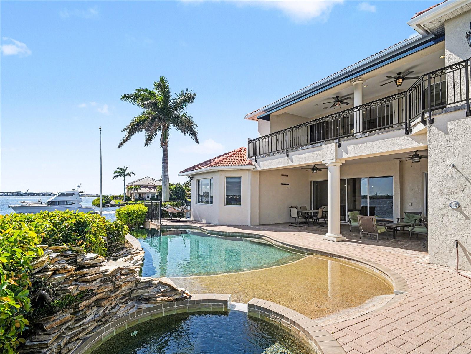 Welcome to an exceptional waterfront estate, gracefully positioned at the end of a palm-lined cul-de-sac on a private peninsula within the exclusive gated community of Riviera Dunes. Set along the peaceful Manatee River, this residence captures breathtaking sunset views and offers a refined coastal lifestyle with convenient access to the Gulf of Mexico via the community’s deep-water marina. This furnished custom home spans over 4,400 square feet of elegant living space and more than 5,700 total square feet designed for both luxurious everyday living and grand-scale entertaining. From the moment you arrive, the paver driveway, striking curb appeal, and three-car tandem garage with designer checkerboard flooring set the tone.  Inside, expansive tray ceilings with ambient lighting, custom ironwork, and timeless finishes create an elevated  yet inviting atmosphere. A grand formal dining room is perfect for hosting, while the massive great room, anchored by a gas fireplace and custom built-ins, offers both comfort and style. The gourmet kitchen is thoughtfully appointed with granite countertops, natural wood custom cabinetry, a walk-in pantry, built-in desk, wet bar, and premium appliances including Thermador and Sub-Zero. The main-level owner’s suite is a private sanctuary, featuring serene water views from every window, a custom walk-in closet, and a spa-inspired bath with glass shower, dual vanities, abundant storage, private commode with bidet, and an in-suite wet bar. Upstairs, a spacious family and recreation area with kitchenette opens to an expansive balcony overlooking the water, ideal for relaxing or entertaining. Step outside to your private waterfront retreat, where a covered patio and seating area lead to a stunning beach-entry, heated, saltwater, infinity pool, perfectly positioned to take in spectacular sunset views over the river. Built for both beauty and peace of mind, the home features hurricane impact glass, a concrete seawall, and has experienced no flooding during recent storm events, an exceptional benefit for waterfront living. Additional highlights include a wine cellar, tile flooring throughout, stucco exterior, and a classic barrel tile roof. While this property does not include a private dock, Riviera Dunes offers one of Southwest Florida’s safest deep-water harbors, with boat slips often available for purchase separately, providing convenient boating access to the Gulf in approximately 10 minutes. This home is ideally located just minutes to I-75, approximately 45 minutes to Tampa International Airport, 30 minutes to Sarasota-Bradenton International Airport, and close to premier shopping and dining at Ellenton Premium Outlets and University Town Center. This is more than a home, it’s a rare opportunity to experience waterfront living with unmatched sunsets, elegance, and privacy.