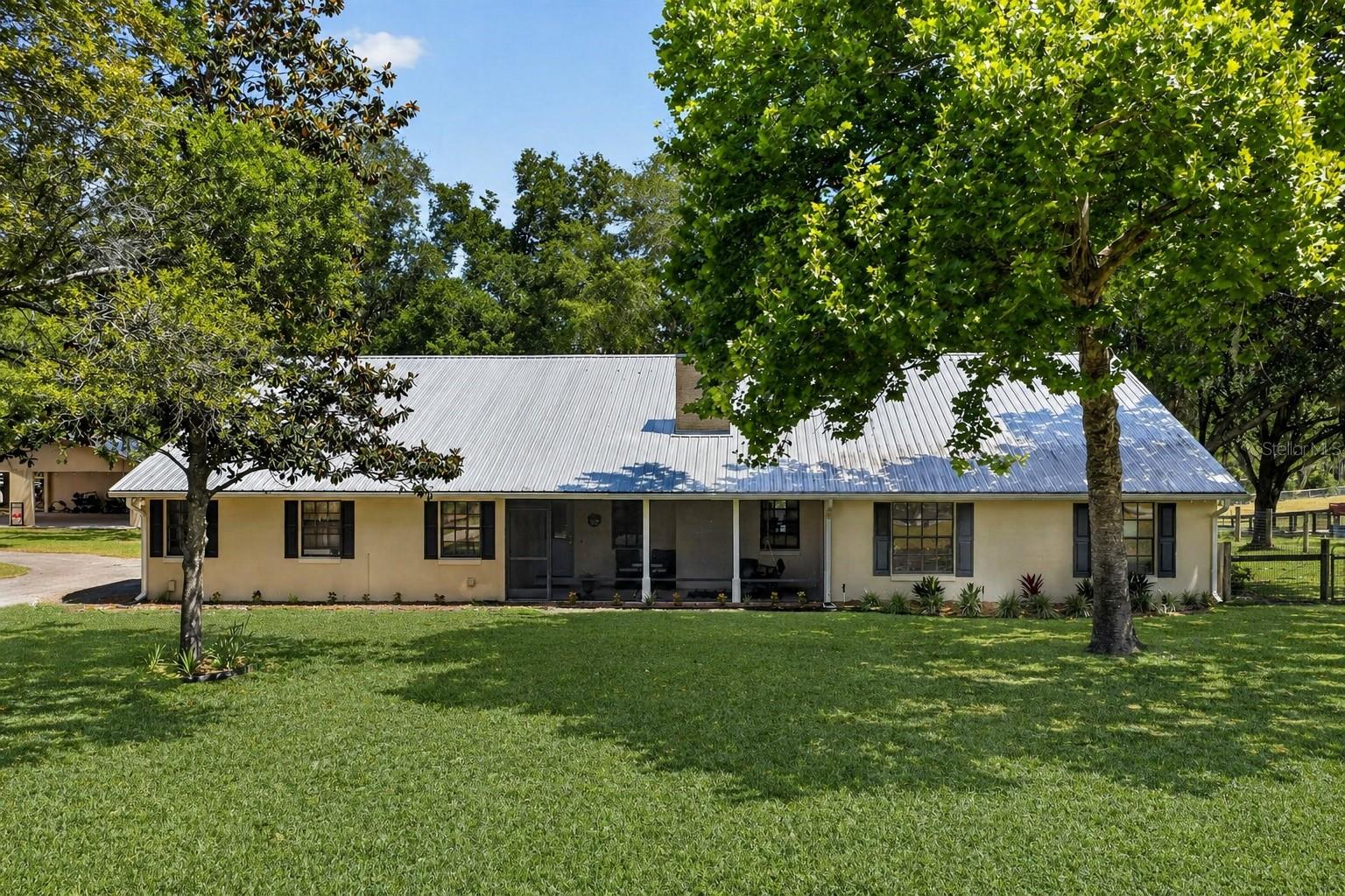 One or more photo(s) has been virtually staged. Dreaming of one day owning a 7.5 ACRE homestead or horse farm complete with a beautiful screened in POOL? A peaceful retreat where you can spend your days and nights enjoying all the things that nature has to offer? Welcome to 11241 Em En El Grove Road. This stunning 4 bedroom 2.5 bathroom home boasting a little over 3,000 sqft of living space is perfectly positioned in the center of gorgeous rolling hills, big shady oak trees, as well as a stunning view of the pond. This is truly a one-of-a-kind home where horses, donkeys, chickens, goats, cows, you name it, are always welcomed with open arms. If farm-life is on your bucket list and you realize that HOA's are over-rated, then you've stopped at the right place!!. This POOL HOME sits ON 7.5 ACRES of pure serenity and bliss- This custom home was updated in 2018 with wood-like tile flooring in the kitchen, family room, hallways & dining room. The interior was freshly painted and recessed can lights were added plus TRIM & DOORS. The master bathroom has a fantastic VANITY, honed marble floors, updated shower w/TILE , beautiful fixtures, and big closets. The hallway bathroom has a vanity w/double sinks, honed marble floors, tub/shower tile and also serves as the pool bath. All bedrooms have spacious closets with closet fixtures. Relax & entertain on your pool deck overlooking the peaceful pond. The back half of the attached two-car garage was converted into a storage/canning room. The large over-sized interior laundry room has enough space that storage racks are able to be utilized. The Property is fully fenced with 3 large pastures and 3 smaller paddocks. For additional entertaining space there is a formal dining room & formal sunken living room with stained concrete floors and a striking fireplace adding a modern element. The kitchen has plenty of wood cabinets, gorgeous tiled backsplash, refinished counters, and newer appliances that were all replaced in 2019 along with the double oven. The kitchen also features a large pantry, breakfast bar and is precisely located in the center of the home making it a fabulous place to gather. Kitchen conveniently opens up into the family room making it a perfect space for everyday casual living. The large kitchen window opens up and overlooks the pool area and large covered patio making this such a functional outdoor living space which is exceptional for entertaining family and friends. French doors lead to the screened pool area from the dining room, the family room and primary bedroom. A huge covered and partially enclosed all block workshop/storage area was built next to the house in 2021. The metal roof was installed on the home in 2019. One HVAC system was replace in 2019 and the 2nd HVAC system was replaced in 2026. The well was replaced in 2019 as well as the septic drain field. The hot water heater was replaced in 2019. The property also has a 3-stall barn (one stall with an attached paddock area) A large 24X12 storage shed utilized as a Feed/Hay/Tack room, Property also has a covered 3-horse wash rack plus 2 separate wells. The property thick tree-line and heavy forage area were extensively cleared creating a picturesque backdrop and view of strategically placed Spanish Moss Oak trees which conveniently create the perfect amount of shade during the Florida summers.