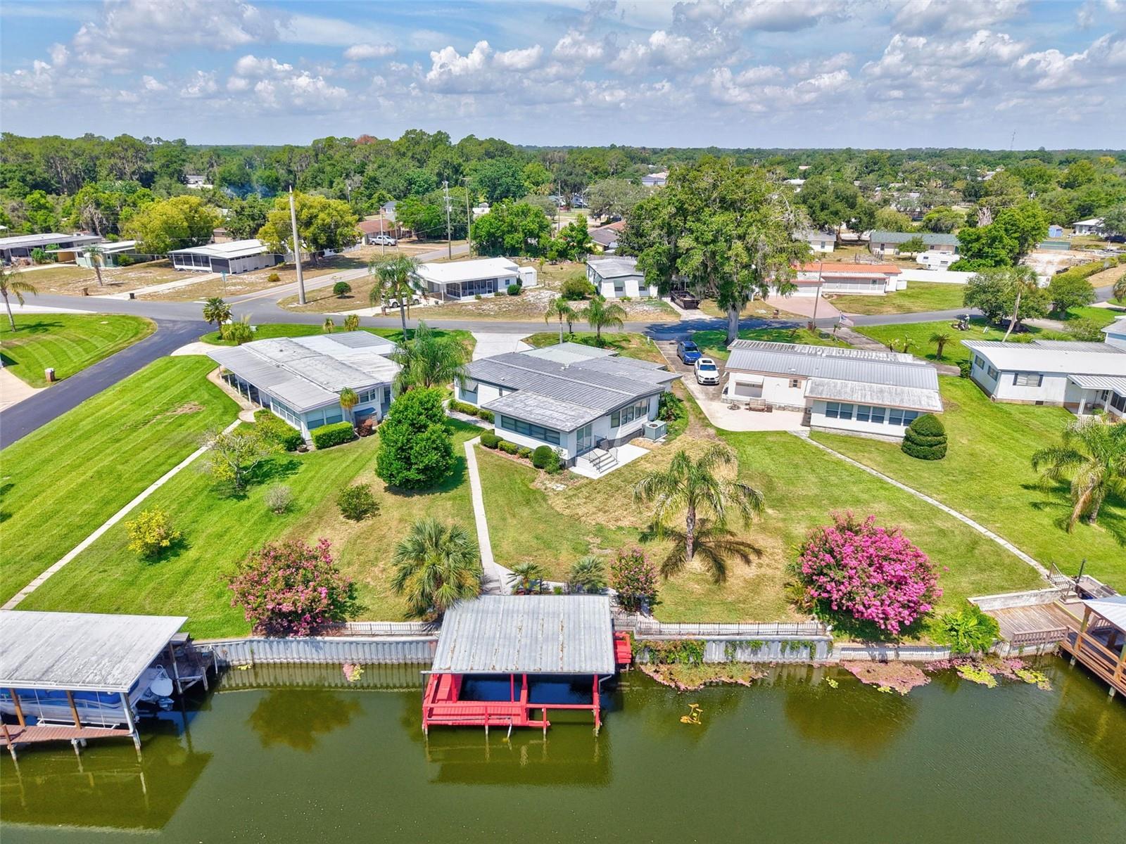 HARRIS CHAIN OF LAKES HOME! It’s time to enjoy what Central Florida living and lake life has to offer. This 1,400+ sq ft, 2/2 canal front home on .24 acre, in a quiet, tucked away, 55+ community (with a low HOA) on Lake Eustis, is ready and waiting for you! You can enjoy winter or summer sunrises in the large Florida Room overlooking the canal and lake, or relax with a cool drink to watch sunsets from the front screened porch, all the while being entertained by the flora and fauna that Lake County, Floridians still enjoy. You will have your own dock and boathouse so you can jump in your boat and ride just 3 minutes by freshwater canal to pursue the premier fishing that the seven lakes on the chain have to offer. From your car or boat, you can shop, dine, sightsee, enjoy walking trails and festivals in Leesburg, Mt Dora, Tavares or Eustis! Moving in will be easy here because there’s so much room for storage! Extra closets, three outside sheds with shelving and 2 work benches, a laundry room with a cabinet, and an oversized driveway with room for visiting friends to park, as well as a golf cart parking area! This home has had so many updates and renovations made since 2019 that you can move right in and breathe easy. Luxury vinyl flooring throughout, bathrooms updated (tile showers and granite countertops), paint (inside and out), plumbing (inside and out), electrical updated to accommodate home, RV and boathouse, irrigation, microwave and Bosch dishwasher (still under warranty), blinds, light fixtures, some doors and windows and more! Call for your private showing!