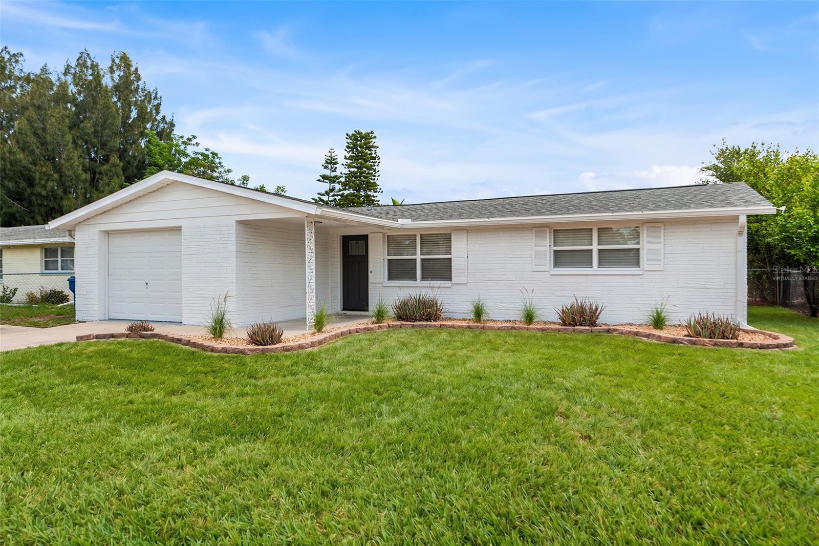 One or more photo(s) has been virtually staged. This solid concrete block ranch home offers three bedrooms, two bathrooms, and a one-car garage, all situated just minutes from US Highway 19 and a short drive to the charm of downtown Tarpon Springs and the world-famous Sponge Docks. The freshly painted white exterior with updated landscaping beds and a bold black front door delivers immediate curb appeal, and the foyer entry sets the tone with clean lines, tile flooring, and a set of glass French doors leading directly into a versatile flex room perfectly suited as a home office, den, or third bedroom. The oversized dining room connects to the main living areas with an open pass-through and offers generous space for large-scale entertaining. The kitchen is well-equipped with solid wood cabinetry extending to the ceiling, dark laminate countertops, a tile backsplash, and a full stainless steel appliance package including a side-by-side refrigerator with ice and water, electric range with built-in microwave, and dishwasher. The expansive living room is a standout feature of the home, boasting a distinctive painted wood plank ceiling and a wall of sliding glass doors that fill the space with natural light and provide direct access to the rear patio and fenced yard. The attached garage is exceptionally deep at over 23 feet, features a utility sink, an automatic opener, laundry hookups. It's ideal for a workshop, hobby space, or future conversion. A full  fence encloses the rear yard and a concrete patio provides the foundation for outdoor living. With easy access to US-19 for commuting throughout Pasco and Pinellas counties, proximity to the beaches of the Gulf Coast, and just a quick trip to the waterfront dining and cultural attractions of Tarpon Springs, this home offers a practical and well-located lifestyle at an exceptional value.