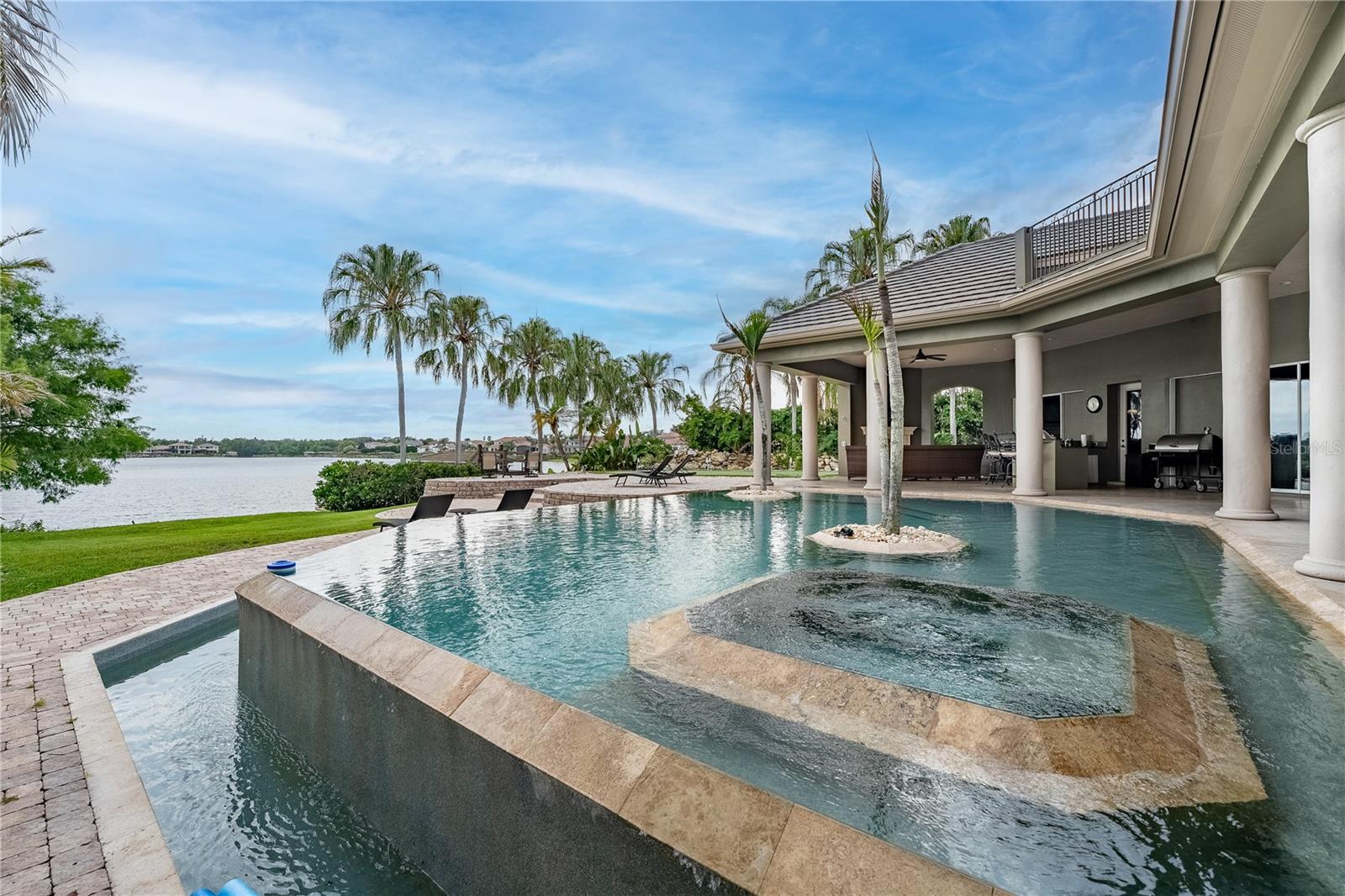 Presenting this stunning LAKEFRONT RESIDENCE showcasing spectacular PANORAMIC VIEWS and ideally located within the premier GUARD GATED COMMUNITY of Reserve at Belmere in WINDERMERE. The property is approached by a circular driveway with centerpiece WATER FOUNTAIN set in mature landscaping alongside an adjoining 3 car garage with side entry. Upon arrival, an impressive entryway opens to the foyer and formal living/great room with seamless glass windows framing picture perfect water views. Set over two floors, this CUSTOM-BUILT home (exterior re-painted 2024) perfectly balances grand entertainment spaces with intimate everyday living featuring soaring ceilings alongside rich architectural artistry with its ornate detailing and trim. The sizeable wood paneled EXECUTIVE HOME OFFICE is a masterpiece with its custom cabinetry, wood floor and ceiling treatment. The GOURMET KITCHEN with high-end stainless-steel appliances and granite countertops has an open floor concept flowing effortlessly into a sunlit breakfast nook, countertop seating and spacious family room with focal point fireplace and sliding doors providing direct access to the outdoor area. A formal DINING ROOM, a BILLIARD ROOM with WET BAR also provide further spaces for entertaining both family and guests. The primary bedroom suite is a true RETREAT with sweeping views and sitting area with direct patio access, two large walk-in closets and ensuite bathroom which includes a walk-in shower, tub and dual sinks. A guest bedroom with full ensuite and two further bedrooms with Jack & Jill bathroom suite are also situated on the first floor. Upstairs, the dedicated HOME THEATER with full bar opens up to an adjoining GAMES ROOM with access to a private balcony providing an additional vantage place to avail of the breathtaking sunrises and sunsets. Also on this level is a HOME GYM workout space. [Note: This upstairs area is VERSATILE as could be utilized as a secondary primary suite as there is also a full ensuite bathroom with large walk-in closet]. Nestled on the shores of Lake Whitney and with its own PRIVATE DOCK, enjoy Florida living at its finest in this PRIVATE OASIS with its resort style outdoor area highlighted by a bespoke VANISHING EDGE POOL WITH WATER FOUNTAIN AND INTEGRATED HEATED SPILLOVER SPA (re-surfaced and new pool equipment 2024). There is an expansive covered lanai with plentiful lounge and dining spaces, an outdoor fireplace in addition to a full outdoor kitchen with countertop seating. A GOLF PUTTING GREEN sits to one side of the patio area and a SERENE GARDEN AREA to the other. The residence is in close proximity to the clubhouse and the community’s many amenities which include a fitness center, playground and tennis, basketball and sand volleyball courts. Reserve at Belmere is conveniently located just minutes from historic downtown Windermere, local shops, restaurants, the theme parks, major highways and nearby top-rated schools. THIS ISN’T JUST A HOME, IT’S A LIFESTYLE! Don’t miss out, book your private showing today!