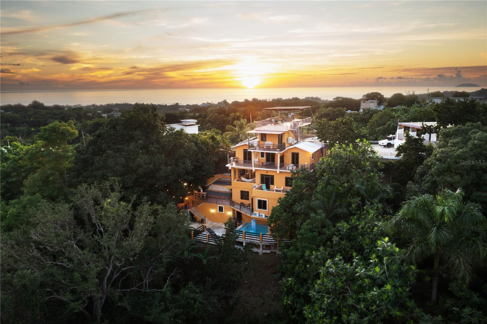 The Terraces at Rincón is a distinctive multi-level hillside property of 8,371 SF designed for strong income performance. Situated on a 418 square-meter lot, it features five private suites across six levels and offers unobstructed 360° views of the Caribbean Sea, the Atlantic Ocean, and Mount Atalaya. Configured to support multi-family use, retreat hosting, and both short- and long-term rental operations, the estate includes five kitchenettes, five full baths, two half baths, two outdoor showers, a laundry area, and parking for five vehicles. Income-driven amenities elevate the guest experience, including a rooftop viewing deck, a jetted spa-style pool with soothing waterfall features, an air-conditioned fitness studio, lush tropical gardens, and multiple outdoor areas for dining, lounging, and quiet reflection. The design thoughtfully blends tropical, Zen-inspired elements with warm Mediterranean and Spanish Colonial touches. Terracotta-style flooring, handcrafted tile accents, stucco textures, rustic wood details, and ironwork railings appear throughout, while expansive windows, open-air corridors, and numerous terraces maximize natural light, ocean breezes, and seamless indoor–outdoor living. The property exudes the charm and serenity of a boutique hillside retreat. Multiple terraces, treetop decks, shaded seating areas, and covered patios create inviting spaces to pause, relax, and savor the signature panoramic vistas. Its elevated setting ensures privacy, tranquility, and uninterrupted ocean-to-mountain views—an experience that resonates with guests seeking both adventure and rejuvenation. Ideally located just minutes from Rincón’s best beaches—including world-famous surf breaks on the Atlantic and tranquil snorkeling coves along the Caribbean—the property also offers quick access to restaurants, the town plaza, grocery stores, and local culture. The combination of prime location, resort-style amenities, and versatile multi-suite configuration positions The Terraces at Rincón as not only a highly desirable investment opportunity but also a place where guests can create lasting memories in one of Puerto Rico’s most coveted coastal markets
