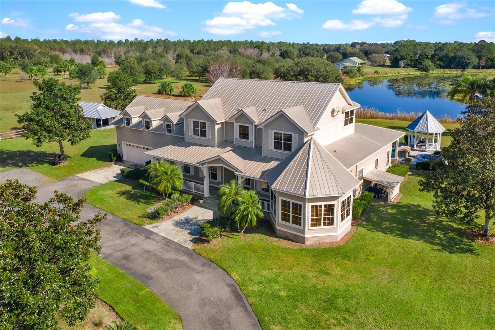 Luxurious contemporary SIX BEDROOM home with RUSTIC FLAIR set on 42 private ACRES, offering a resort-style country retreat. Designed for both work and play, this architecturally distinctive residence features a DEDICATED HOME OFFICE, a gourmet STONE KITCHEN with island cooktop, breakfast bar and poolside access. The adjacent GREAT ROOM with a dramatic stone, wood-burning FIREPLACE captures the central space. Unique living spaces include a turret or CROW’S NEST, balcony, and a versatile IN-LAW SUITE multipurpose bonus room ideal for home-schooling, media, recreation or a second master Bedroom. REVEL in outdoor living with the resort-style pool, sun deck, BBQ area, firepit, gazebo, ENTERTAIN or just RELAX in total privacy. BRING THE HORSES or other farm pets; use the 3 or 4 stall HORSE BARN with ONE BEDROOM APARTMENT!  Offered As-Is, the property is well-equipped with an attached 2-car garage, detached parking structure, multiple bay and pole barn parking for RVs, horse trailers, or boats, and the 3 or 4-stall horse barn with a comfortable, second floor APARTMENT. A horseshoe-shaped, man-made freshwater lake brings sandhill cranes to this scenic setting along including a covered dock.  Additional amenities include a 6,000 sq ft workshop with storage, basketball court and chicken or dog pens. Conveniently located between Orlando, Daytona, and Ocala, walk or ride to Lake Norris Conservation Area, over 3,500 acres of trails for horseback riding, biking, kayaking and hiking. So many possibilities for this location;  LIVE, farm, GROW... maybe agrobusiness? ...Goat Yoga? This is a rare opportunity to enjoy space, privacy, and lifestyle; live the life you’ve imagined.