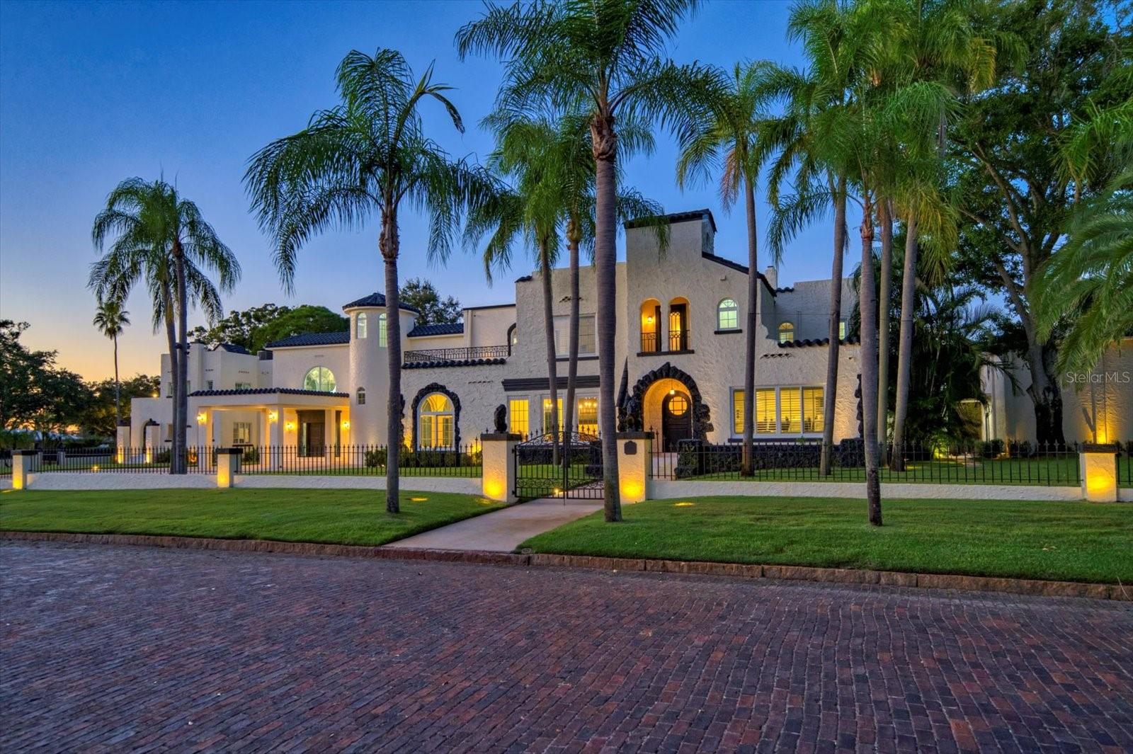 Set within the prestigious Pasadena corridor and adjoining the historic Jungle Prada district, 320 Park St. is one of St. Petersburg’s most distinguished estates. Long known as the “Faith Mansion,” this gated property—once a sought-after setting for weddings and elegant events—has been transformed into a refined modern residence where timeless architecture meets effortless contemporary luxury.

A sweeping circular drive and porte-cochère lead into a striking 23-foot entrance hall crafted in high-polished black-and-white marble, illuminated by impact-rated Pella windows. It’s graphic, elevated, and instantly memorable—an editorial-quality backdrop that feels both classic and current.

Beyond the foyer, the grand ballroom unfolds with coffered beams, plaster walls, and two sparkling crystal chandeliers. Designed for large gatherings yet equally suited to quiet evenings, the space balances drama with serene, livable elegance.

The estate offers two beautifully planned kitchens. The west-wing chef’s kitchen features a sculptural custom range hood, commercial Z-Line gas range (in both kitchens), dual pantries, wine refrigerator, and a substantial island with a sleek passthrough to the dining hall. A separate banquet kitchen supports hosting at any scale with ease.

The primary suite is a tranquil retreat with plantation shutters, a sitting area, dual walk-in closets, and a morning bar. Its marble-wrapped bath includes double vanities, a soaking tub, and a remarkable 140 sq. ft. walk-in shower with multiple showerheads. A lofted lounge overlooks the foyer and ballroom with architectural presence.

The entertainment wing includes tin ceilings, a custom copper penny–topped bar, a wine cellar, and a private 8-seat theatre with a 115” retractable screen, Optoma projection, surround sound, and reclining leather seating. Every bedroom is ensuite.

Behind the scenes, the home has been comprehensively modernized: new roofs, seven HVAC zones many with dehumidifiers, full electrical rewiring, new irrigation and landscape lighting, new pool pump, Generac generator, impact windows, and dual hot water systems—all contributing to comfort and peace of mind.

Outdoors, the PebbleTec pool and redesigned terraces offer multiple areas for dining and lounging. The outdoor kitchen includes a gas grill, Big Green Egg, sink, and generous prep space. The grounds feature Zoysia grass, irrigated raised garden beds, and fruiting trees including mango, Meyer lemon, fig, avocado, Asian pear, and lime.

Connected via a covered breezeway, the property’s flexible auxiliary spaces include a 1,200+ sq. ft. garage structure with epoxy floors, industrial-grade doors, gym area, separate golf cart garage, and an attached 1-bedroom, 1-bath apartment with kitchenette—ideal for an au pair, guests, multigenerational living, or a private office/studio.

Lighted walkways, pedestrian gates, and two drive-in gates enhance the estate’s sense of arrival. With downtown St. Petersburg, Treasure Island, and the Gulf beaches only minutes away, this estate delivers elegance, ease, and architectural poise.

A home of scale, beauty, and impeccable composition, 320 Park St. invites you to live each day with the elevated style of a magazine-worthy estate.