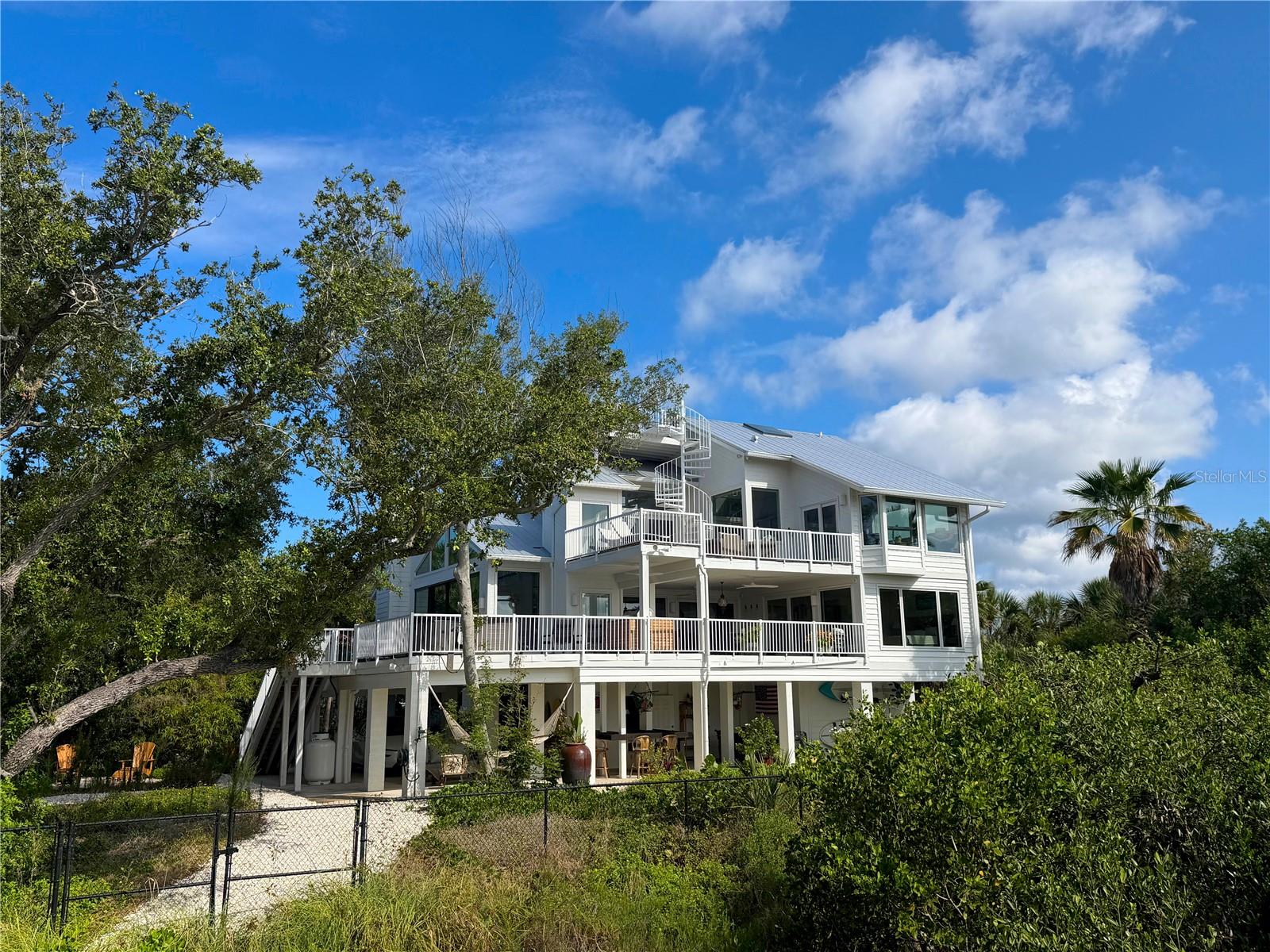 Rare bayfront acreage with deeded Gulf beach access on Manasota Key. Hidden behind a gated entrance and nestled among majestic live oaks, native palms, and lush tropical landscaping, this extraordinary coastal property offers a level of privacy and natural beauty seldom found on the island.

Designed to embrace its surroundings, the custom residence offers approximately 3,806 square feet of living space and more than 2,000 square feet of outdoor living areas. Expansive impact-rated windows and doors frame water views and fill the home with natural light, while premium European cabinetry, custom built-ins, and thoughtfully curated architectural details create an atmosphere that is both timeless and inviting.

The main living level opens seamlessly to an expansive covered lanai finished with porcelain tile that continues from the interior living spaces, creating effortless indoor-outdoor living. A spacious main-level suite with bay views, direct lanai access, custom closet systems, and a beautifully appointed bath provides exceptional flexibility for guests or multi-generational living. Upstairs, the primary suite enjoys direct access to the upper-level deck and rooftop observation deck, where panoramic views of Lemon Bay, the Intracoastal Waterway, and the Gulf of Mexico create an unforgettable backdrop.

Outdoor living is a defining feature of the property. Multiple levels of gathering spaces include covered and open-air decks, a ground-level entertainment pavilion, outdoor fitness and recreation areas, and a 10' x 8' spa. A private boardwalk winds through the natural shoreline landscape to the water's edge, connecting a series of waterfront destinations and a bayfront platform overlooking Lemon Bay.

Ownership includes natural shoreline areas and submerged lands extending into Lemon Bay, creating a unique private waterfront setting rarely found on Manasota Key. Deeded Gulf beach access is located directly across the street, offering the best of both worlds—sunrise views across the bay and sunsets over the Gulf.

Additional features include impact-rated windows and doors, high-efficiency mechanical systems, extensive insulation and air sealing, tankless propane water heating, and a landscape carefully preserved to enhance privacy, beauty, and connection to the surrounding environment.

Whether entertaining beneath the live oaks, enjoying the rooftop views, relaxing by the water's edge, or strolling the private boardwalk, this is a property that offers an experience as unique as its setting.