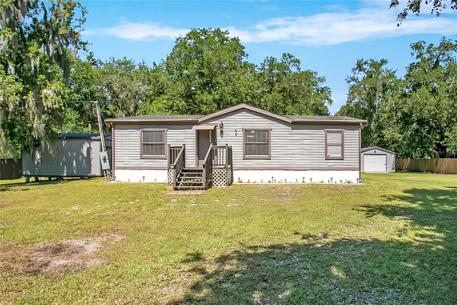 No HOA. Bring your boat, your RV, your trailer, your toys. This is .77 acres where you park what you want, when you want. This home is well maintained and move-in ready, backed by recent upgrades that matter. New roof in 2019. A new tankless water heater and new water softener. New deck and new skirting, both done in 2025. LVP flooring runs throughout most of the home. The home also comes with a 2026 engineering report already in place covering the tie-down straps. Set up your RV without the runaround. The property includes a dedicated RV hookup and pad wired for both 30 amp and 50 amp service. Step inside to an open kitchen and living room built for the way you actually live. White cabinets, stainless appliances, and a tile backsplash give you a kitchen that works as hard as you do. The living room stretches wide enough for movie nights or Sunday football, no negotiating for space required. Retreat to your primary suite after a long day. Your bathroom includes a tiled walk-in shower. Two more bedrooms give you room for kids, guests, or a home office you've been meaning to set up.
Step outside and the lot takes over. Mature oaks drip Spanish moss over almost three-quarters of an acre, giving you privacy most Orlando properties can't touch. A spacious deck sets the stage for your next cookout. An oversized shed with a roll-up door and established electricity gives your tools and projects a real home, alongside a separate detached garage and additional storage. This is what space feels like when it's yours to use. Come see it for yourself.