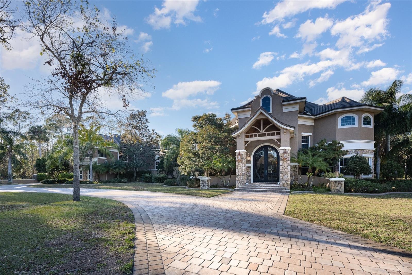 Step into a world of unparalleled luxury with this custom-built estate in the heart of Port Orange, crafted by the late Frank Baker of Baker Homes. Priced to sell immediately, this home epitomizes the best in quality, location, subdivision and excellent school system. Baker, a visionary in energy efficiency and sustainability since 1977, ensured every project met the highest standards of quality and craftsmanship. The millwork in this home is exceptional. The multi-dimensional tile roof, which essentially refers to a roof that can generally last for 50-100 years due to the durability of tile materials, making it one of the longest-lasting roofing options available. Enter through the grand 8-by-12-foot custom iron doors and step into the 26-by-31-foot foyer, featuring a grand split staircase leading to the second-floor catwalk. A second staircase off the family room and kitchen add to the home's convenience. The estate boasts six bedrooms, six full baths and two half baths, with the first floor adorned in luxurious marble flooring. The four-car garage with marble and connected by a breezeway includes a billiards room, media room and bar, ideal for entertaining. The separate guest house offers a living room workout room, downstairs full bath, steam room, washer and dryer, upstairs bedroom with separate bath, and private balcony overlooking the pool. The air-conditioned space of guest room and billiards/media room is not included in the home's square footage. On a sprawling 2.4-acre lot with an adjacent pond and conservation area, this home is surrounded by a concrete-wrought iron perimeter wall with two gates for entry to the expansive paver circular drive. The massive foyer with chandelier, fieldstone columns and crown molding sets the tone for the rest of the home, where ceilings in the main living areas range from 20 to 23 feet, featuring tray, coffered and domed designs. The main house includes five bedrooms, with three en suites and two bedrooms sharing a Jack and Jill bath, an office, plantation shutters, laminated solar glass impact windows, gourmet eat-in kitchen with a full appliance package and dedicated pantry, propane tank and custom laundry room. The primary suite offers a private balcony overlooking the pool and lanai, two custom-designed walk-in closets and a luxury bath. The expansive dining room is ideal for entertaining large parties. The custom pool is like no other, with a hot tub and separate pavilion with a fireplace, all enclosed in a majestic structure built to withstand strong winds. The substantial covered lanai areas are ideal for outdoor Florida entertaining, and the outdoor summer kitchen off the guest house is ideal for hosting functions. Car enthusiasts will appreciate the marble-floored four-car garage measuring 22 by 52 feet. The billiards room and media room above the garage are separated by a custom bar, ideal for entertaining. The home features two separate living areas, a living room with fireplace, 21-foot coffered ceilings and floor-to-ceiling windows, and a family room off the kitchen that opens up to the outdoor lanai and pool area, ideal for entertaining. Every bedroom has a custom walk-in closet. This custom home offers everything a distinctive buyer desires such as quality construction, outdoor living space, ample garage storage, elite baths, high ceilings, floor-to-ceiling windows, outdoor lighting, laundry rooms and walk-in wardrobes. Don't miss the opportunity to own this Port Orange estate.