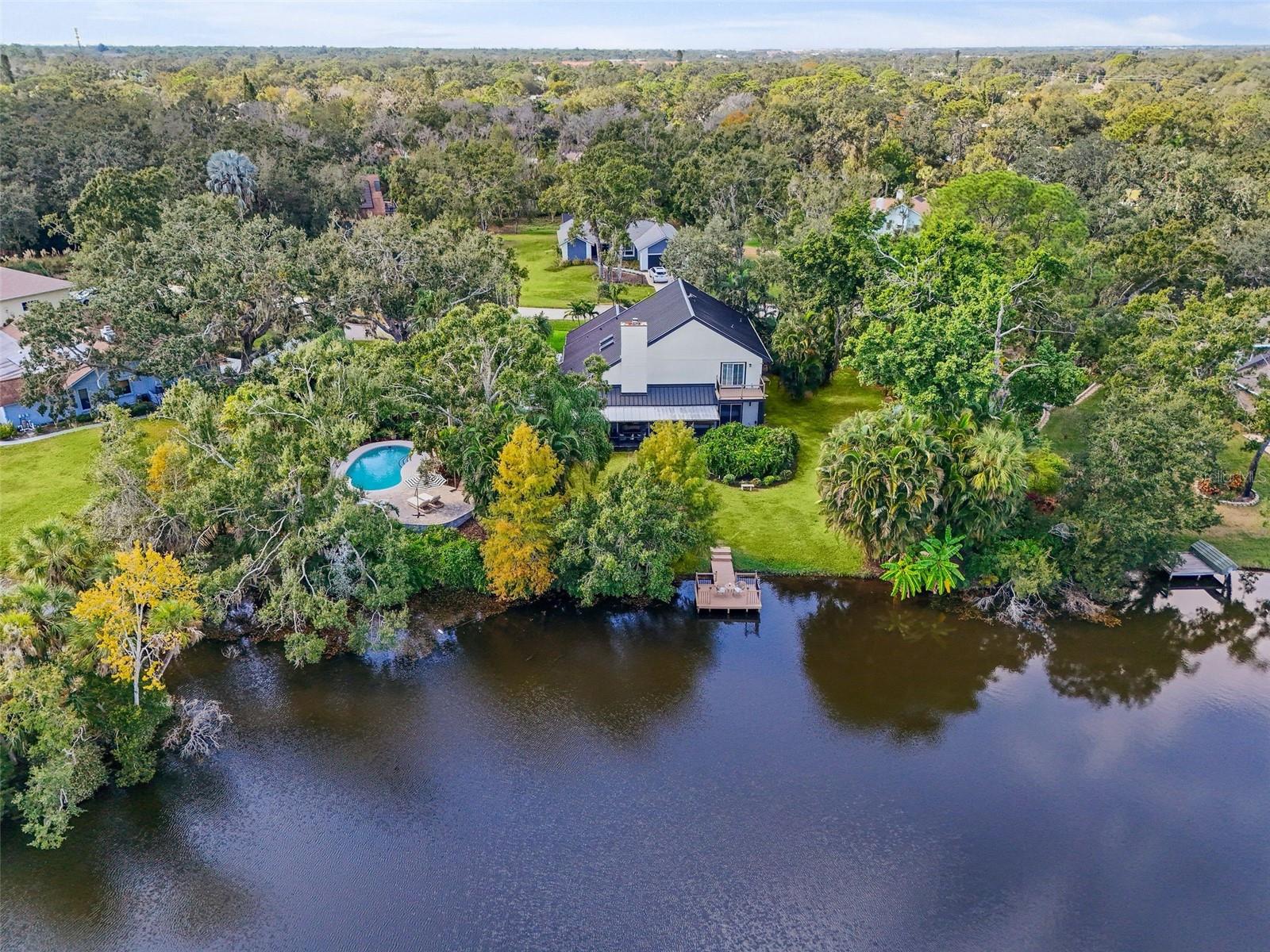 Tucked away on the tranquil cul-de-sac of Ravenwood Way, this architecturally rich home blends European elegance with modern, thoughtful design. The 1-acre waterfront estate is designed for gathering, entertaining, growing, creating, and living beautifully.  Upon entry you are met with soaring 27-foot cathedral ceilings in an open, free-flowing floorplan ideal for entertaining. The space has Canadian white oak engineered floors, offering warmth against the sleek black accents, natural cement touches, and refined marble details found throughout.  The chef-inspired kitchen is a distinctive statement — truly crafted, using German engineering principles, intelligent design storage, and premium integrated appliances. A striking 16-foot cement waterfall island, created by local artist Jake Brady, captures the spirit of the home — artisanal, durable, and functional. The kitchen features a 48" AGA British induction stove, dual Fisher & Paykel built-in fridge & freezer, elegant pot filler, Italian Elica Arrezzo ventilation system, two Asko stainless steel dishwashers, and an appliance garage. Off the kitchen is the relaxing bay-window breakfast nook. The living area, with a fully functional wood-burning fireplace, creates an atmosphere of intimate gatherings. Adjacent is the TV projection room — a cozy retreat designed for shared experiences. The staircase's modern single-piece aluminum railing enhances the home's architectural lines. The first floor main suite, features a custom white oak privacy wall, dedicated workspace nook, and thoughtfully designed walk-in closet with white pine industrial-style storage. The main bathroom continues the aesthetic: double vanities, soaking tub, shower, and soft neutral design. Upstairs, the two bedrooms were both designed with comfort in mind — sliding closet doors, built-in storage, one with a window seat, and the other has a private balcony overlooking the lake. The second-floor landing, ideal for a study, office, or creative space, serves as a vibrant corner for kids, professionals, or guests.  The upstairs bathroom embraces a refined black-and-white marble theme. The downstairs half-bath is a true conversation piece featuring a living wall, one-piece violet marble sink imported from Turkey, and a technologically advanced toilet with heated seat, handless flushing, and luxury finishings. Three sets of French doors open to the L-shaped covered lanai, transforming indoor living into outdoor lifestyle. Overlooking the lake, private dock, mature trees, and native wildlife. Enjoy the lake while kayaking, pole fishing, or relaxing on a small boat. The saltwater heated pool sits within lush low-maintenance tropical landscaping, framed by Sarasota-native palms, fragrant ginger plants, and fruit trees (mango, banana, pomegranate, guava, & starfruit.  The home offers an updated laundry room, new garage cabinetry and flooring, and additional attic storage. The Ravenwood community is known for its generous lot sizes, architectural individuality, and rapid gentrification. Ideally located close to Nathan Benderson Park (with rowing, trails, world-class events), UTC Town center mall, dining galore and championship golf courses.  It is a short drive to Airport or I-75 for easy commuting and a short drive to Downtown & Sarasota’s world-famous beaches. Secluded, yet minutes from everything that defines Sarasota living.  It is the perfect address for those who value serenity without sacrificing access or lifestyle.