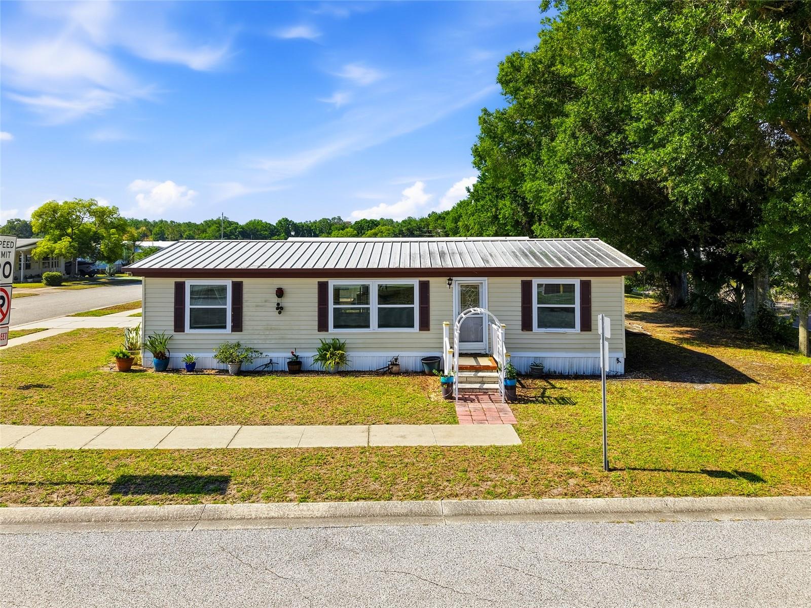 Discover comfortable and affordable Florida living in this well-maintained 3-bedroom, 2-bath home located in a desirable 55+ community in Wesley Chapel. Offering 1,056 square feet of living space with a desirable split-bedroom floor plan, this home features numerous updates throughout, including a newer updated kitchen, newer windows, and stylish vinyl plank flooring in the kitchen, living room, dining room, and laundry room.  The spacious layout provides a nice sized living room, functional dining space, and a convenient inside laundry room. Outside, enjoy the covered carport with a nice closed in storage building, perfect for storing your mower, and lawn tools. Situated on a corner lot, this home also offers great curb appeal.  One of the standout features is the unbeatable location directly across from the community amenities. Simply walk across the street to enjoy the pool, shuffleboard courts, and clubhouse, making it even easier to enjoy the active Florida lifestyle this community offers. Perfect for year-round living or a seasonal retreat, this move-in ready home offers comfort, convenience, and a fantastic community setting.