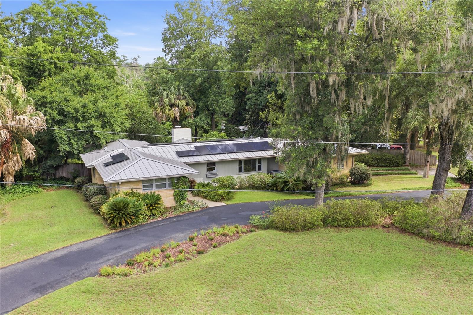 Classic mid-century home nestled in the premier Fl Park neighborhood less than 2 miles from UF! This special, fully renovated home has been lovingly cared for by its owners for over 3 decades. Upgrades include:  24 gauge standing seam metal roof (2023), double paned glass windows & sliding glass door, and 1.5 MKW Solar system! The spacious & bright living room features 12 Ft high tongue & groove ceiling with exposed beams, double sliding glass door leading out to the patio, and a cultured-stone gas fireplace. The music/media room has custom built-in cabinets. The kitchen features custom wood cabinets, Corrian solid counters, a gas cooktop, oven, microwave, SS refrigerator, and dishwasher. Beautiful hardwood floors are in all living areas. The owner's suite features en-suite bath with dual vanities, walk in shower, dual closets, and built-ins. The master bathroom has an electric towel heater and two bathrooms have walk-in showers, and the third bathroom has a cast iron tub. The guest baths are tiled in mint condition. Enormous family/bonus room features, a large skylight, electric fireplace, LVP flooring, extensive built-in bookcases, custom counters, shelving, and a wine cooler. The split floor plan is ideal for a multi-generation family: the family room and adjacent the fourth bedroom have an exterior entrance and would be perfect as an in-law suite. This bedroom has glass block windows. One bedroom is used as an office and has a walk in closet with a digital Liberty safe. LOW utility bills from the 39 solar panels generating 1.5 MHW of power; There is a Tesla Powerwall 2 backup battery with automatic switching in case of power outage. LG Washer/dryer (gas) are included. The detached workshop/storage building is 10’ x 10’ and has 110v power.  Oversized, landscaped corner lot with circular drive is filled with azaleas & palms. A large tiled semi-circular cracked-tile patio features a wood burning grill and hood: Perfect for entertaining. Fully fenced back yard and 12x12 Trex deck that overlooks the wooded urban buffer along Hogtown creek. This Exceptional location is within walking distance to Ring Park, creek trails, schools, shopping, and all NW amenities.