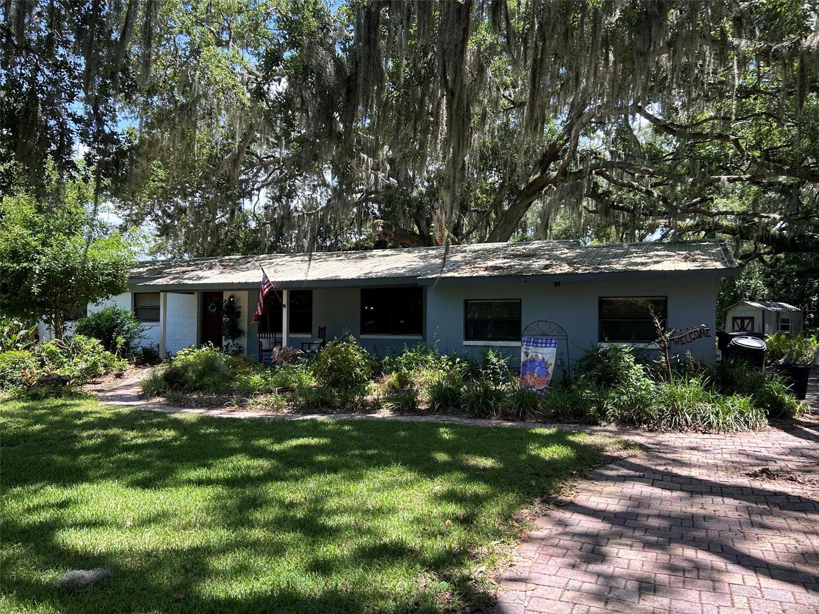 Your dream of country living can be realized!  Just over an acre of property on a peaceful rural road.  Tucked under a canopy of ancient oaks this home is a diamond in the rough with so many possibilities.  Wide open living area as you enter with an open kitchen.  Down the hallway to the right you will find a large room with a walk-in closet. Formerly an art studio this room was plumbed for a sink that can easily be removed.  This room would make a great second master suite with privacy. Its Off to the left from the living room you will find three bedrooms with a large bathroom which was formerly two bathrooms. The room currently being used as an office does not have a closet.  Out in back is a sparkling caged pool with a brick pavered lanai, former rose garden and several sheds for outdoor storage. Recent improvements include new septic drain field, new well  pump and newer pool pump and A/C. The outbuilding has electricity, water and a bathroom.  Its current occupant has transformed it into a tiny home, must be shown by appointment.  You won't find a prettier setting for your country dream. Close to everything but feels like miles from nowhere.