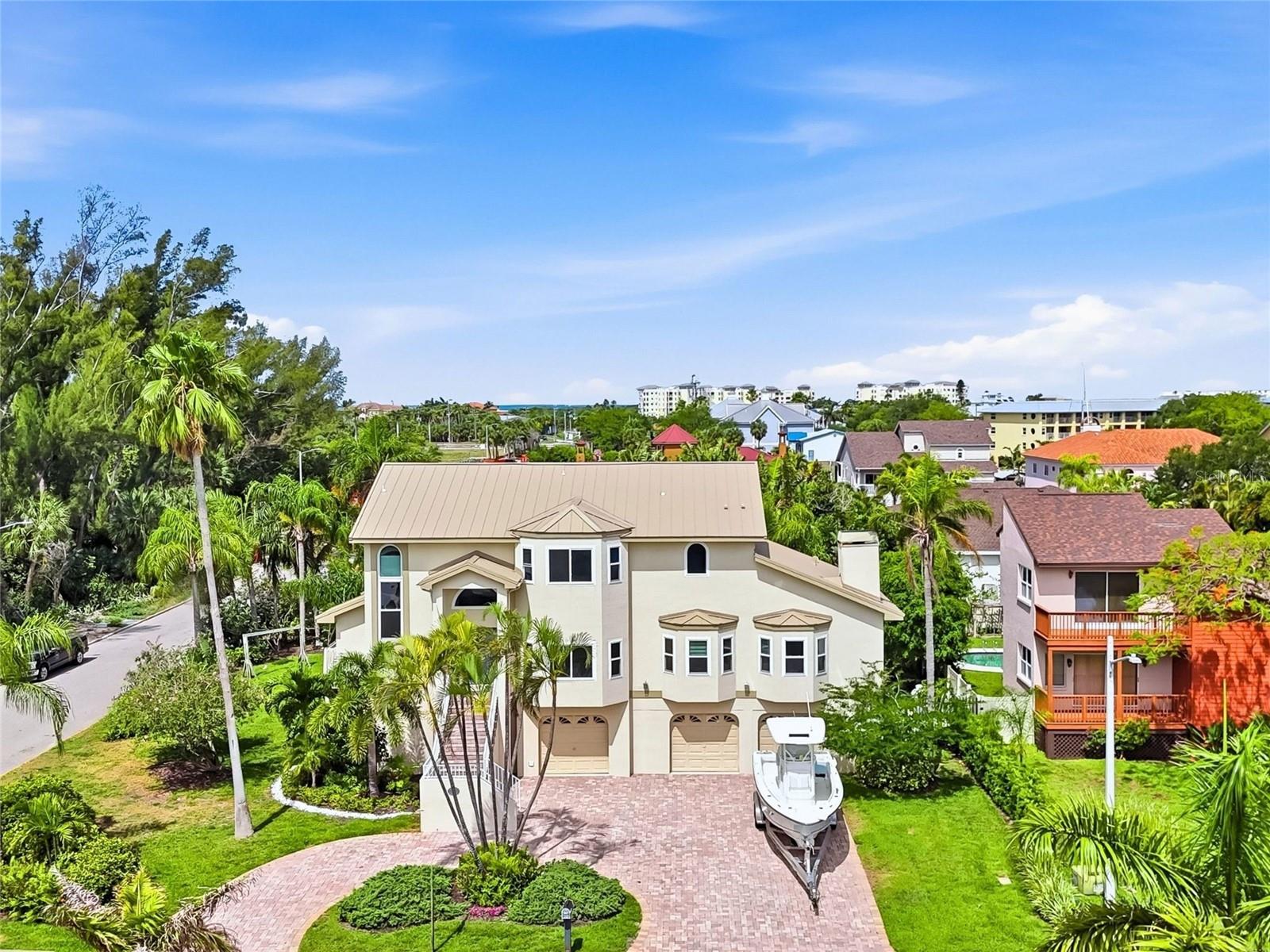 Spacious & elevated Tierra Verde home on an oversized corner lot with a remarkable garage, workshop, and bonus area that provides the kind of versatile space rarely available—ideal for hobbies, car collections, projects, storage, or simply having room to spread out. This four-bedroom elevated residence with BRAND NEW METAL ROOF offers generous living and entertaining spaces, set on an oversized corner lot with plenty of garage & storage space. While not waterfront, the upper levels reveal partial views of Tampa Bay, enjoyed from the new high impact windows and multiple vantage points throughout the home. As you arrive, the oversized circular paved driveway welcomes you home. Ascend the elegant front staircase to the newly installed high-impact rated front door, a great entry point leads into a contemporary, sunlit, open floor plan featuring high ceilings. Thoughtful interior flow seamlessly connecting your formal dining room, spacious living area, and an elegantly freshly updated kitchen with white cabinetry, quartz countertops, pull-out drawers, and new stainless appliances. Large island allows for comfortable breakfast bar seating. The adjoining family room, with its cozy wood-burning fireplace and new window treatments, flows seamlessly to the relaxing outdoor balcony overlooking the lushly landscaped yard and oversize pool. The main level includes a guest bedroom (or office) with adjacent full bath, while the oversized primary suite boasts balcony access, a generous walk-in closet, and a spa-inspired bath with Jacuzzi tub and large walk-in shower. Upstairs, you’ll find two additional bedrooms with its own closets, a full bath, and a secondary living area—ideal for lounging, watching tv or use as a game room. Beautiful views or Tampa Bay from the top floor! The ground floor offers over 2300sf of an impressive multi-car garage ( 4 -6) with workshop, bonus room, and direct access to the pool with spa and shaded patio, creating a perfect space for hobbies or entertaining. Ideally located just 15 minutes from downtown St. Petersburg and close to award-winning beaches and dining, this beautifully maintained home offers the space, flexibility, and lifestyle of true island living.
